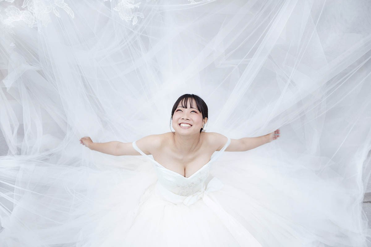 A beautiful Japanese bride is surrounded by her wedding dress as she looks up in happiness.