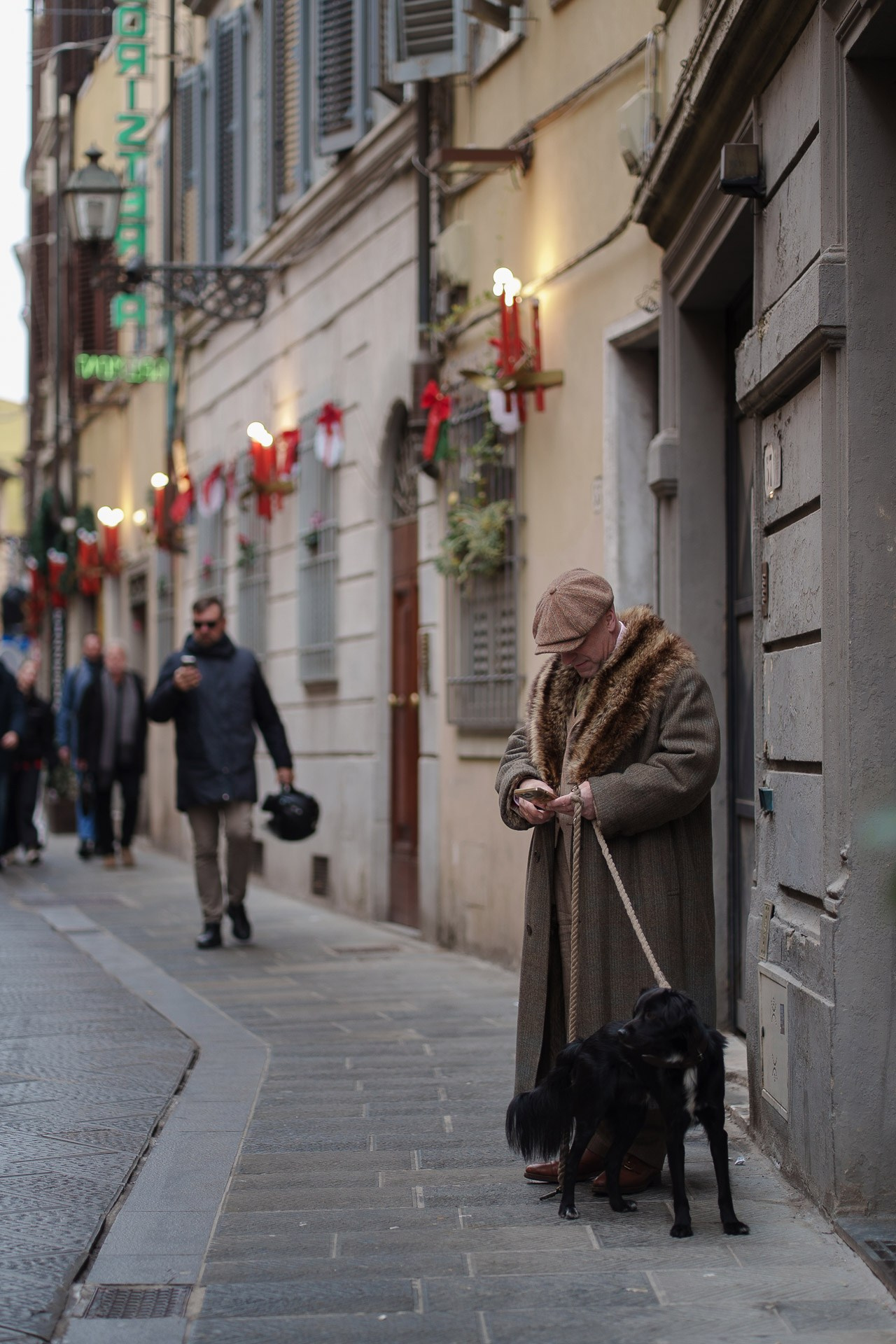 Elderly woman in long coat walking dog on Florence street during Pitti Uomo street style
