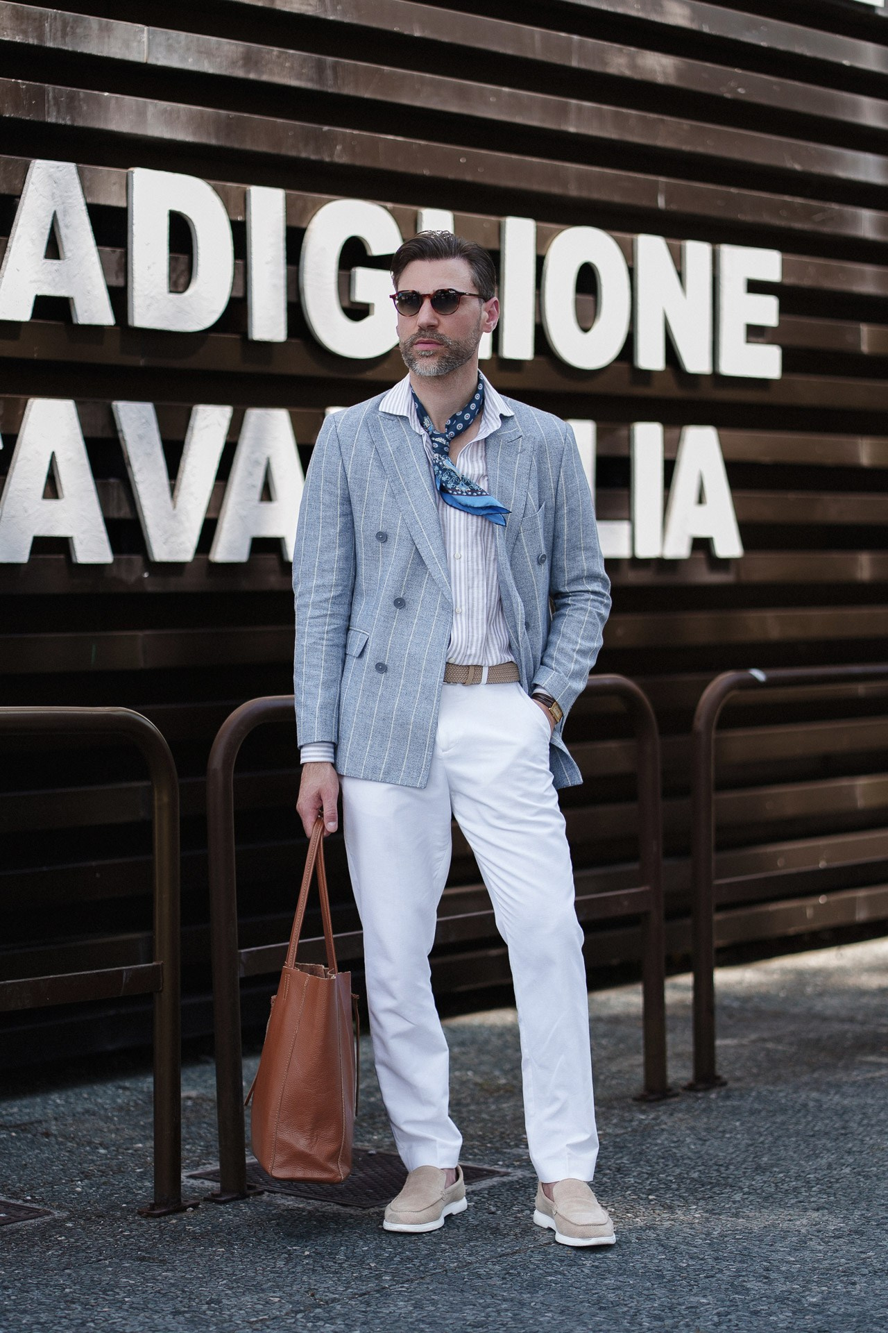 Pitti Uomo 110 guest in blue blazer, white trousers and scarf outside Fortezza da Basso
