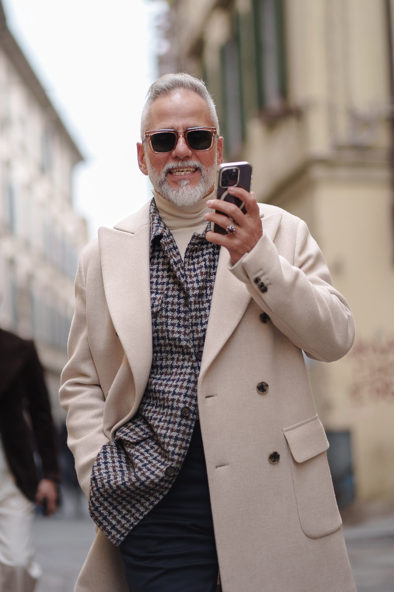 Man in beige coat taking photo with smartphone at Pitti Uomo 109 street style