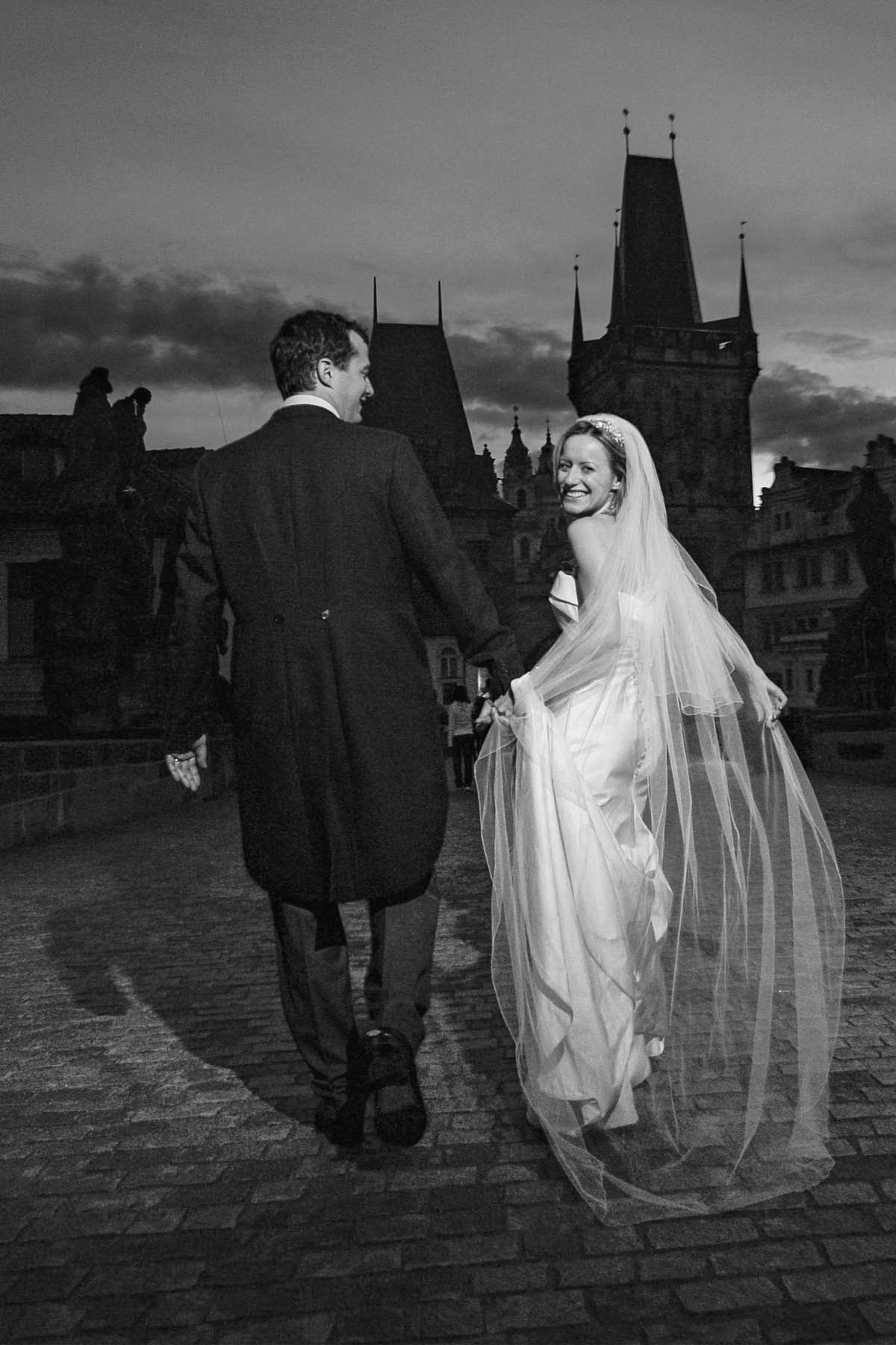 The bride looks back in happiness as she and her husband run across Charles Bridge.