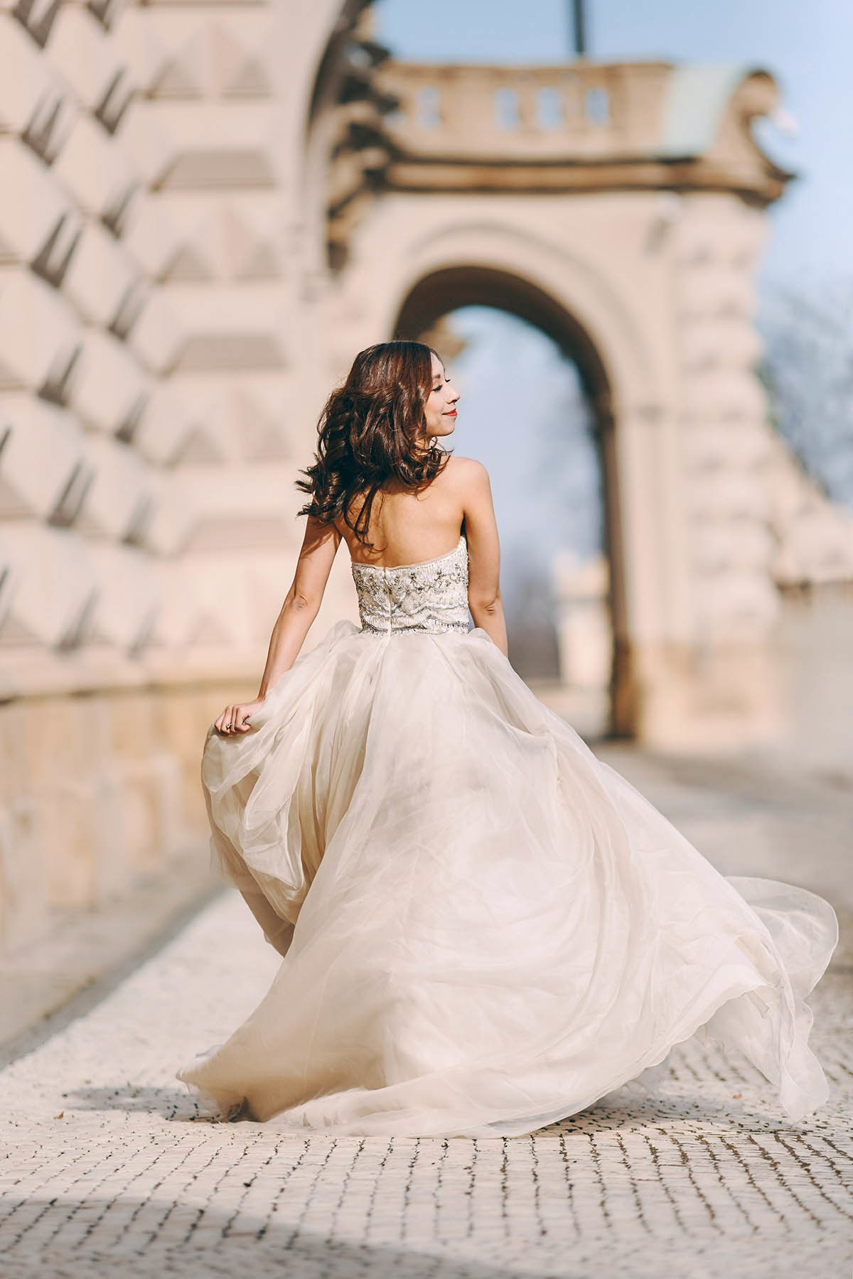 An Asian woman is seen from behing as she struts in her stylish designer gown near a historical palace at Prague Castle
