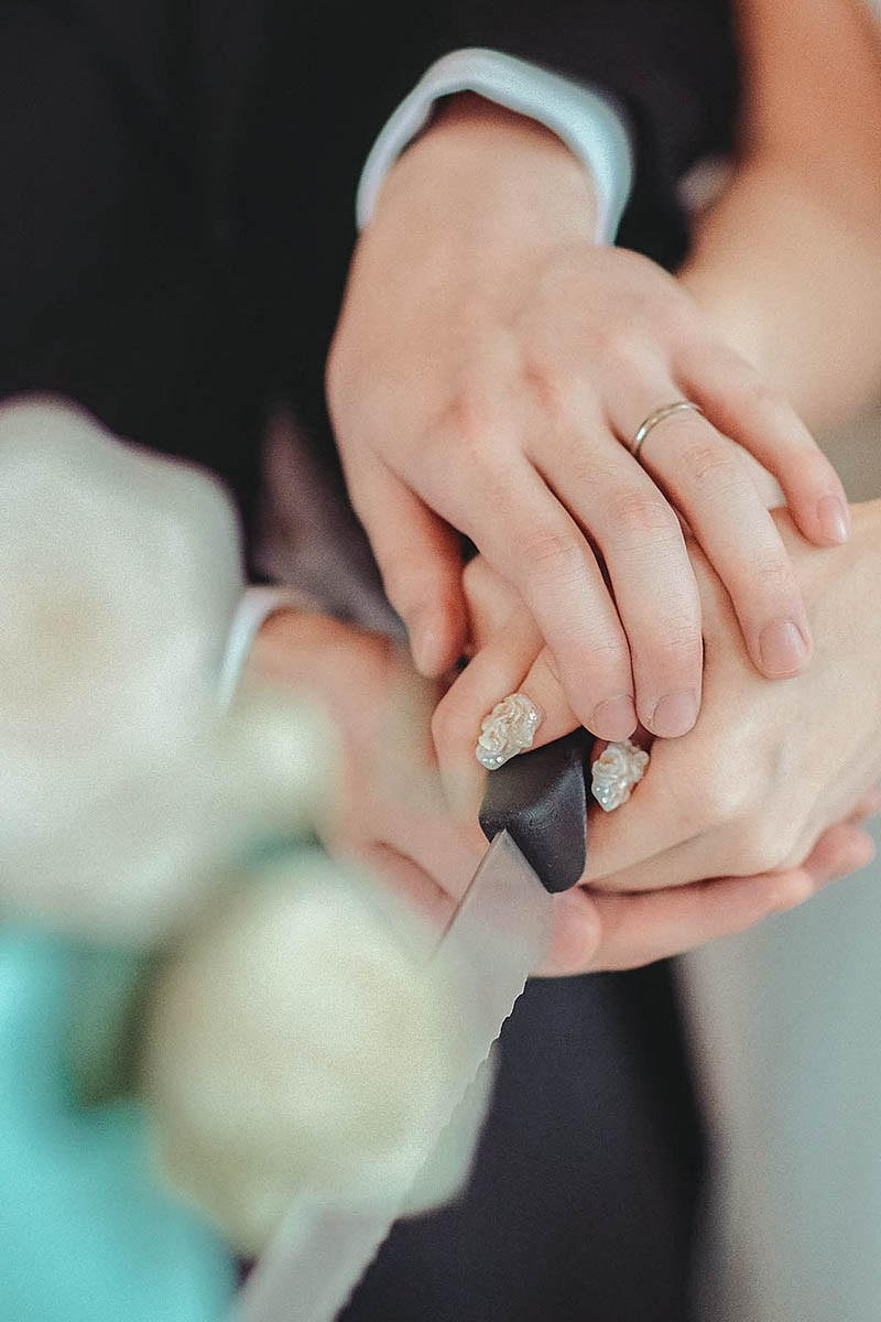 A close-up view of the newlyweds' hands as they cut the wedding cake.