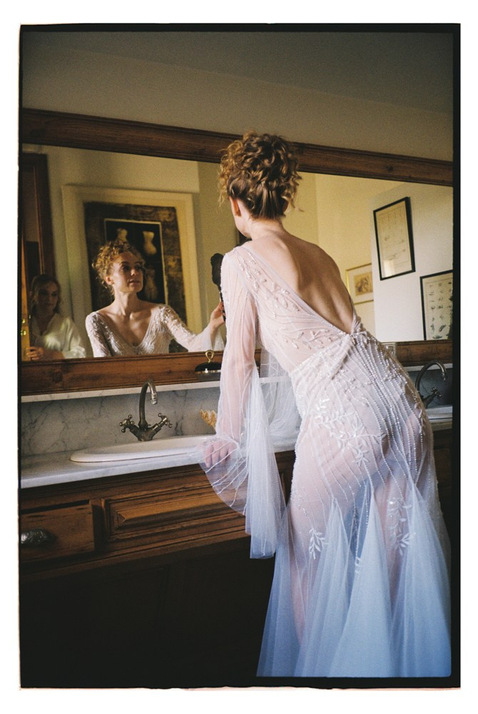 Bride adjusting dress at mirror during wedding preparation in France