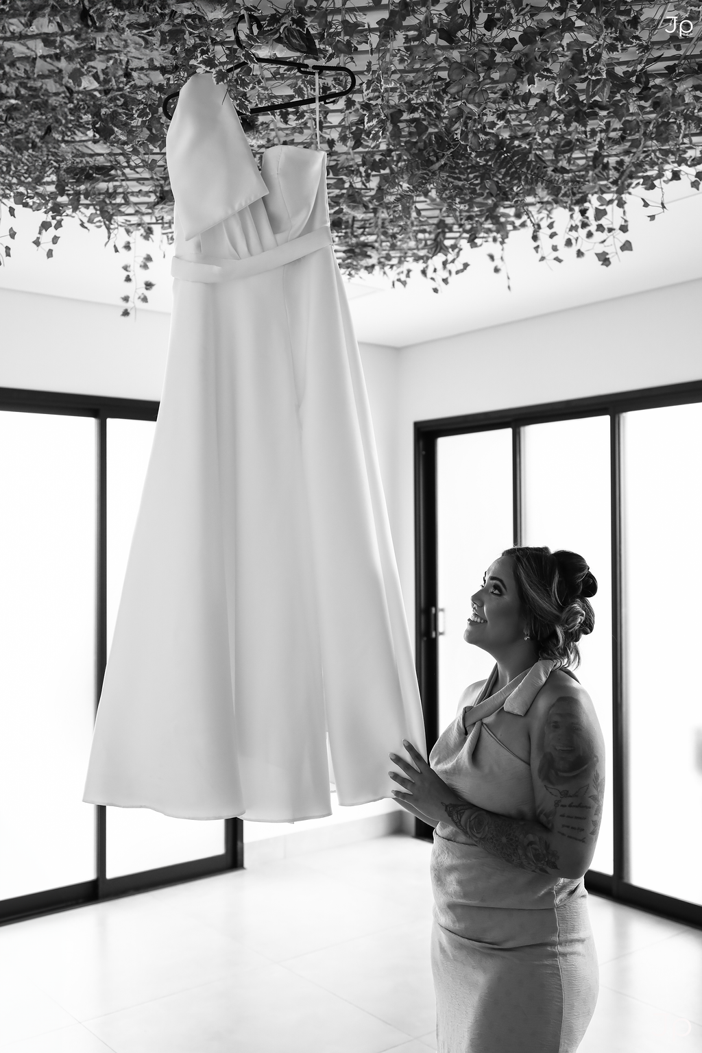 Um vestido de noiva pendurado em um ambiente iluminado com uma cortina branca.