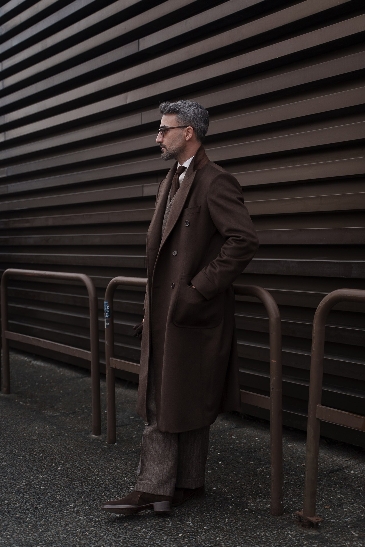 Man in dark brown coat leaning against wall outside Pitti Uomo Florence