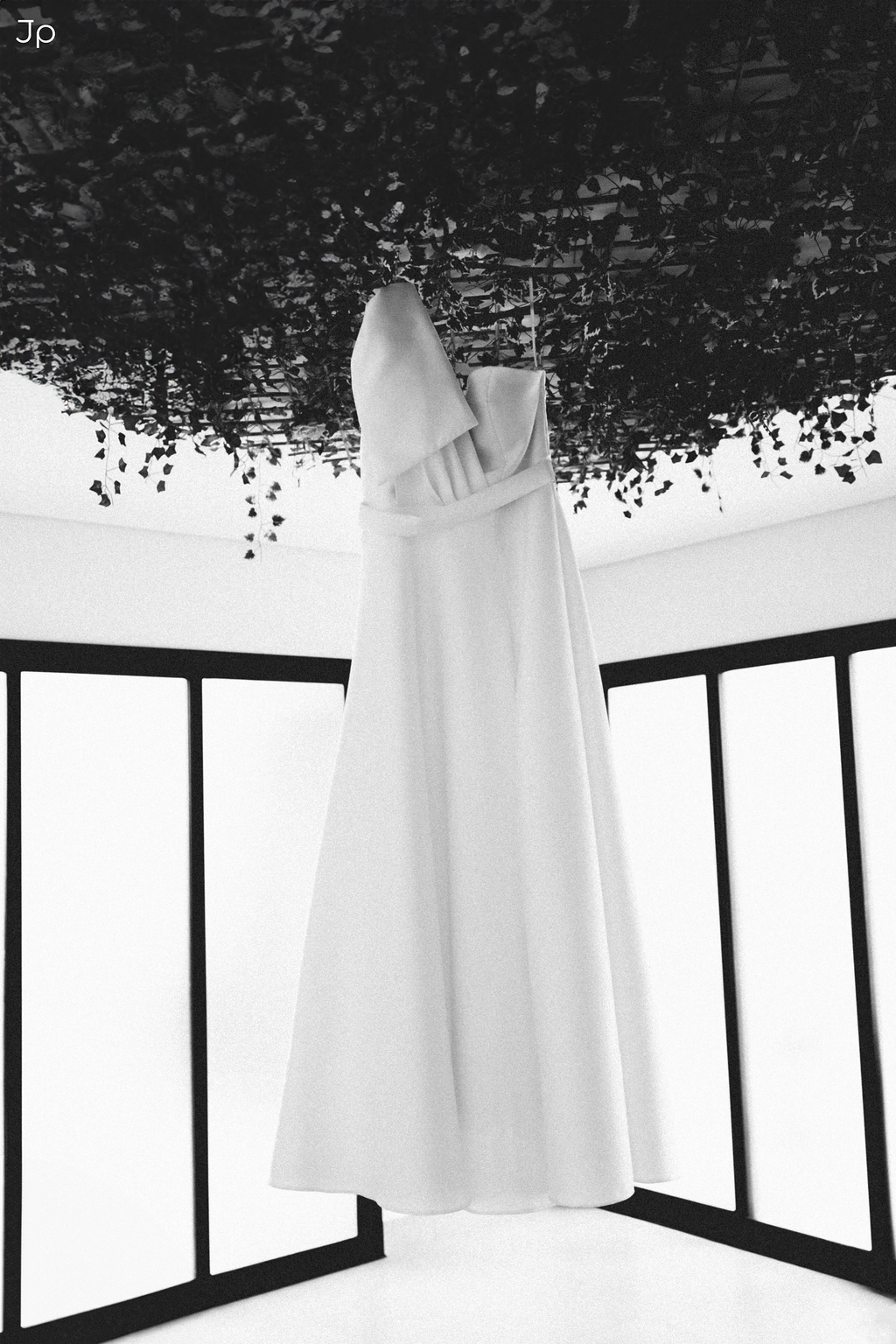 Vestido de noiva pendurado perto de uma janela brilhante.