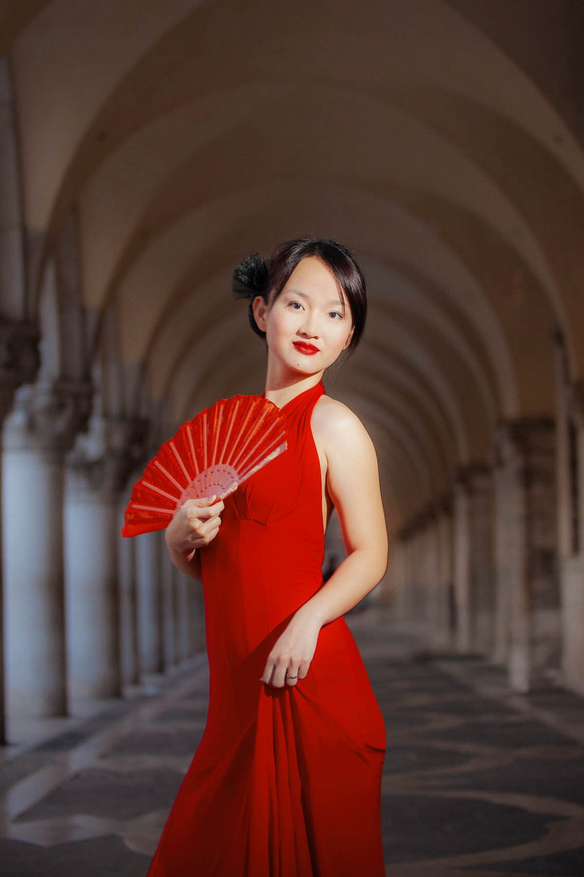 Beautiful Thai woman in slinky red dress holding fan at historic Doge's Palace Venice.