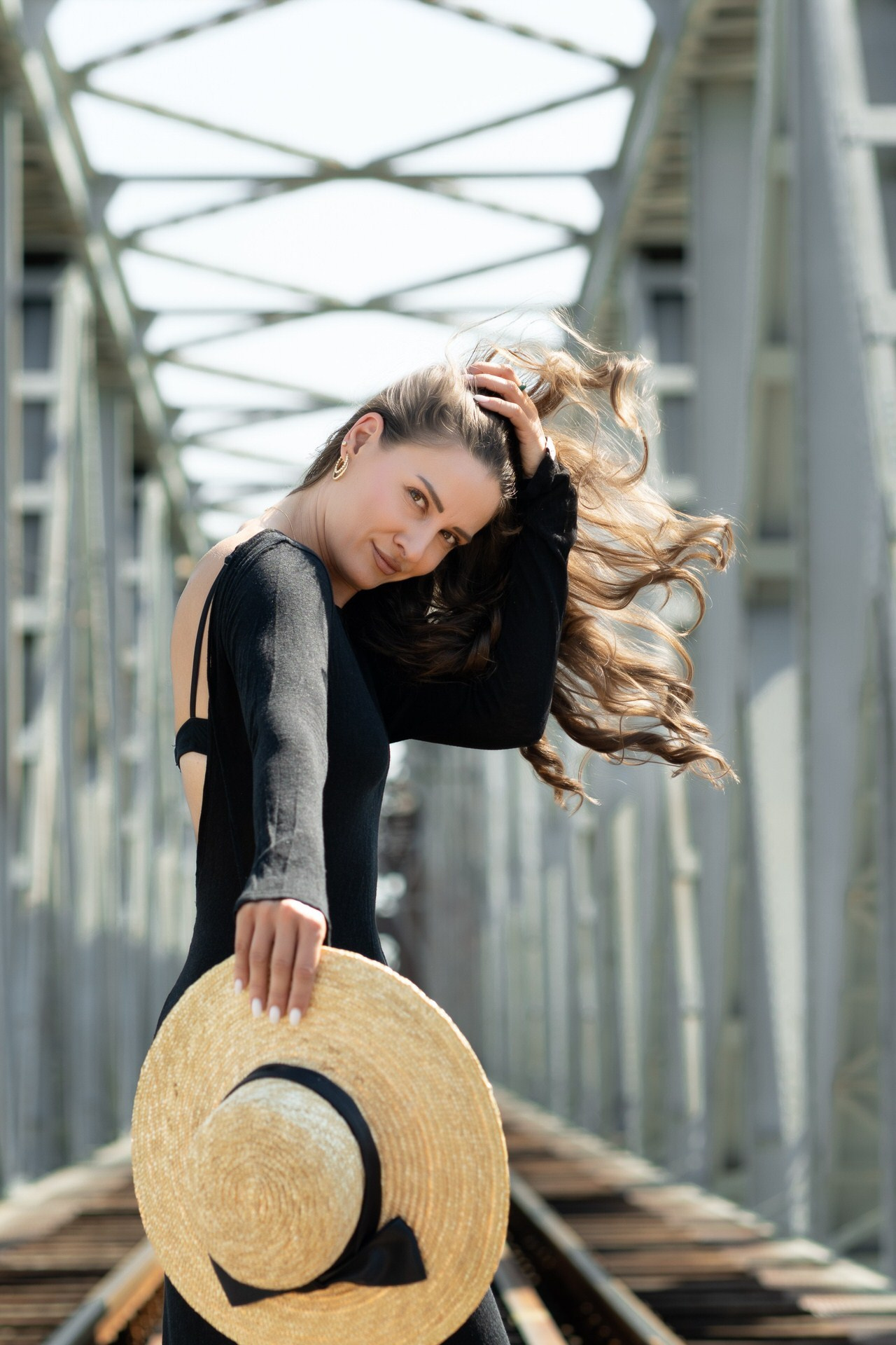 portret devojke koja stoji na starom železničkom mostu i drži šešir u ruci