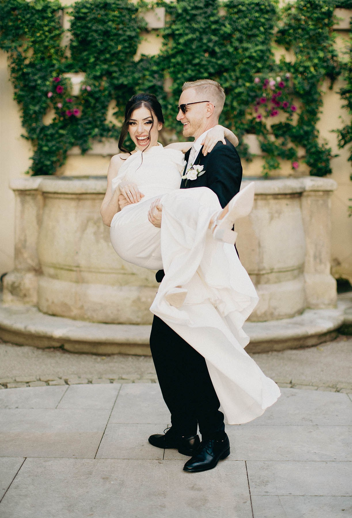 Happy bride laughs as she is spun around by her blonde-haired Czech groom wearing Ray-Ban sunglasses.