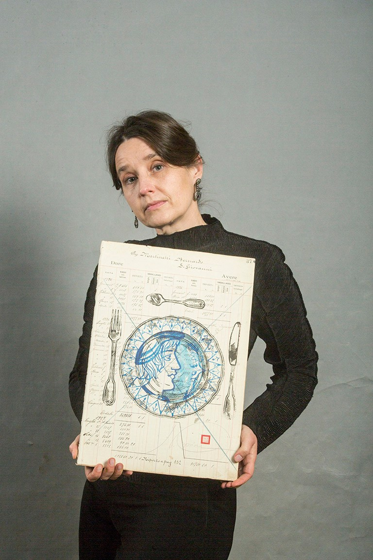 Opera su registro contabile storico (1918–1930) con stampa manuale in linoleografia. All’interno del piatto, un profilo umano dipinto in intenso inchiostro blu diventa fulcro visivo ed emotivo. Il blu dialoga con la carta antica e con il nero della stampa, evocando memoria, intimità e silenzio. Ispirazione ai piatti nuziali rinascimentali italiani, riletti in chiave contemporanea.