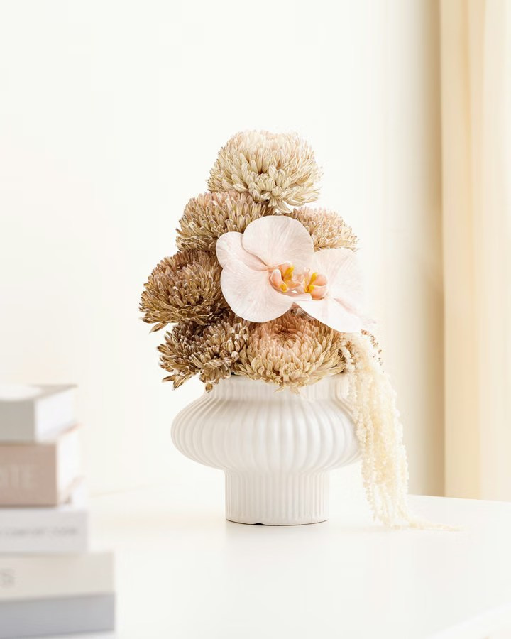 White sculptural vase with dried flowers and an orchid on a neutral background