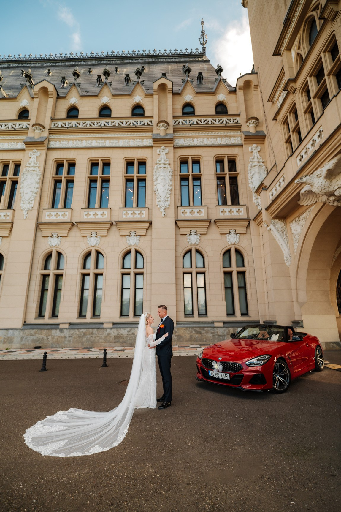 Cuplu de miri langa un BMW rosu in fata Palatului culturii din iasi - Sedinta foto nunta
