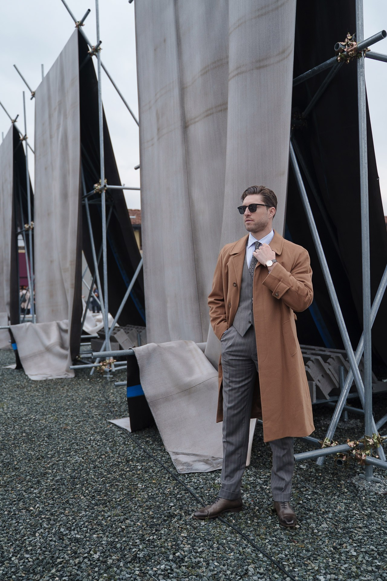 Man in camel overcoat and grey suit posing outside Pitti Uomo 109 Florence