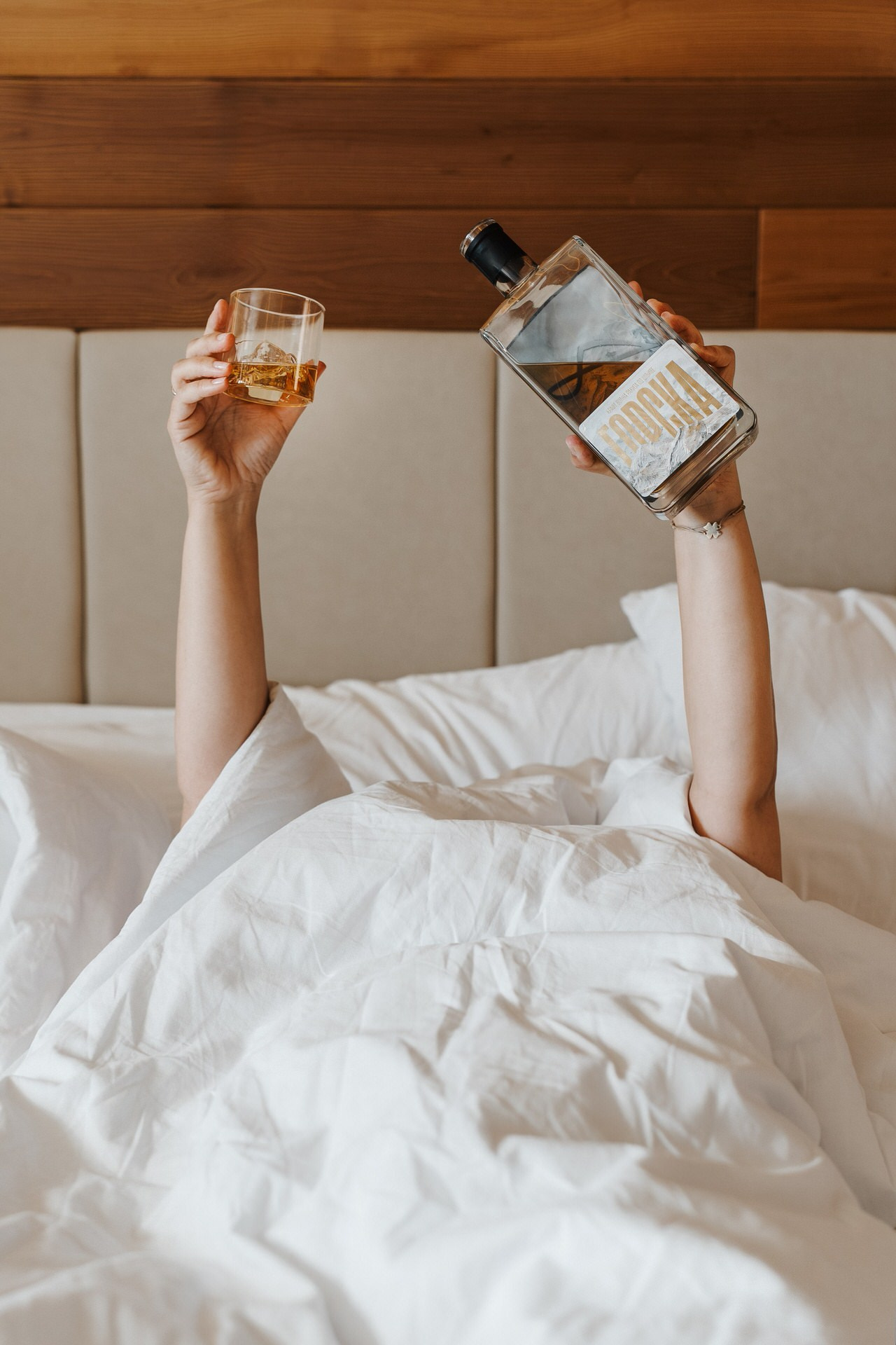 ruke koje vire iz jorgana drže rakiju Gorsku i čašu kao da sipaju 