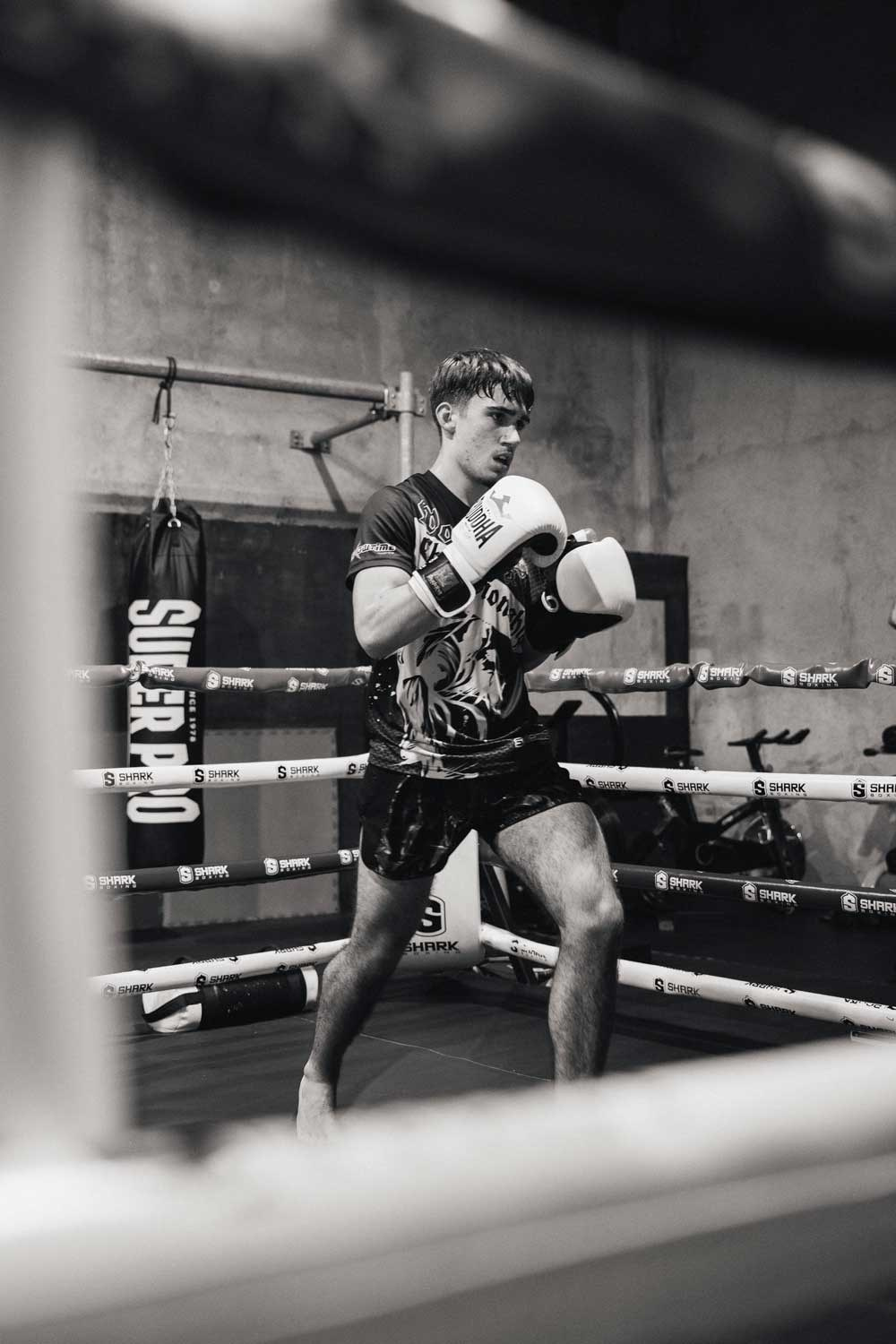 Fotografia desportiva a preto e branco de uma pugilista a dar um soco dentro de um ringue de boxe