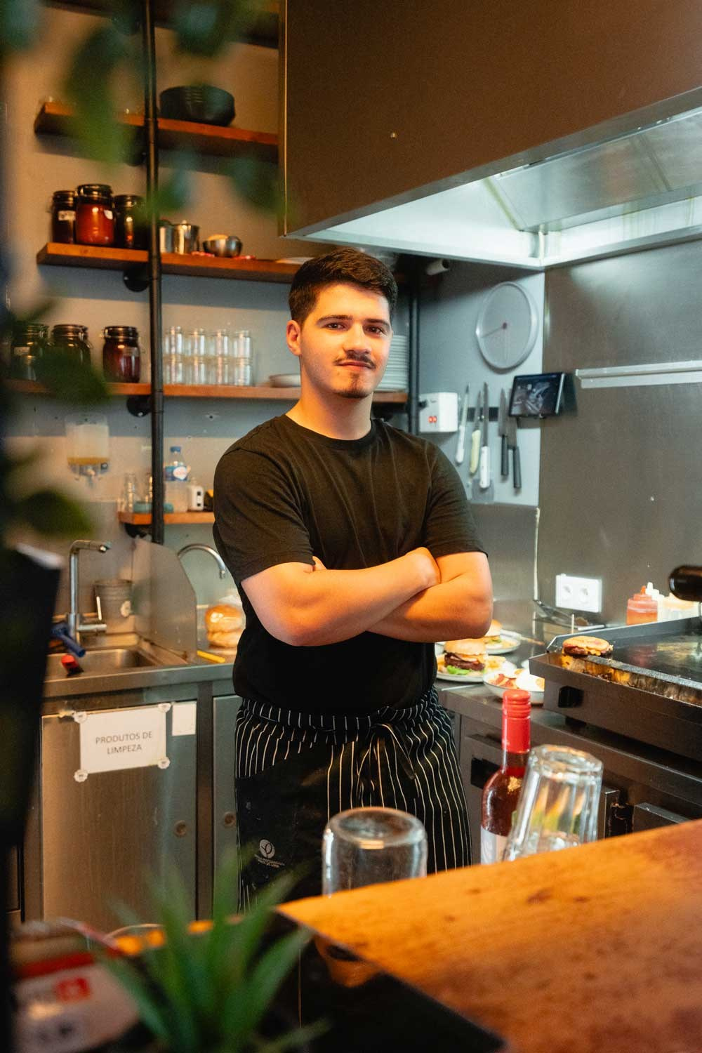 Fotografia corporativa de um jovem chef ou funcionário de braços cruzados numa cozinha de restaurante, captada no norte de Portugal pela Khave Media
