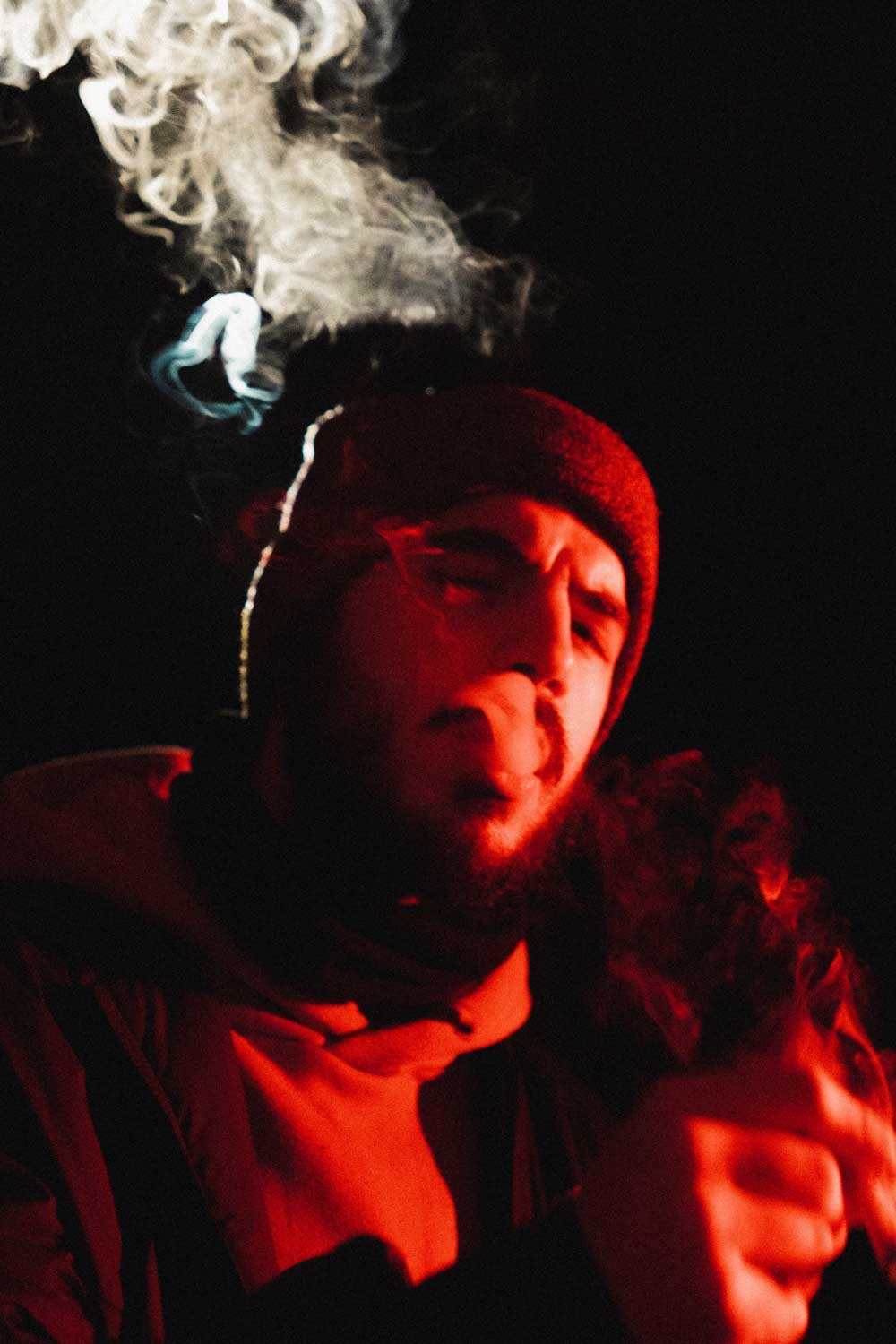Fotografia de retrato criativo de um homem com gorro a exalar fumo sob iluminação vermelha dramática, produzida pela Khave Media