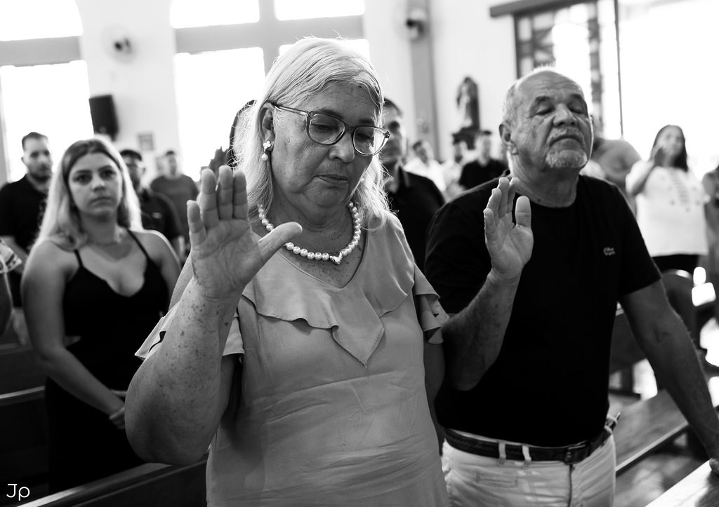Senhora idosa levanta as mãos em oração.