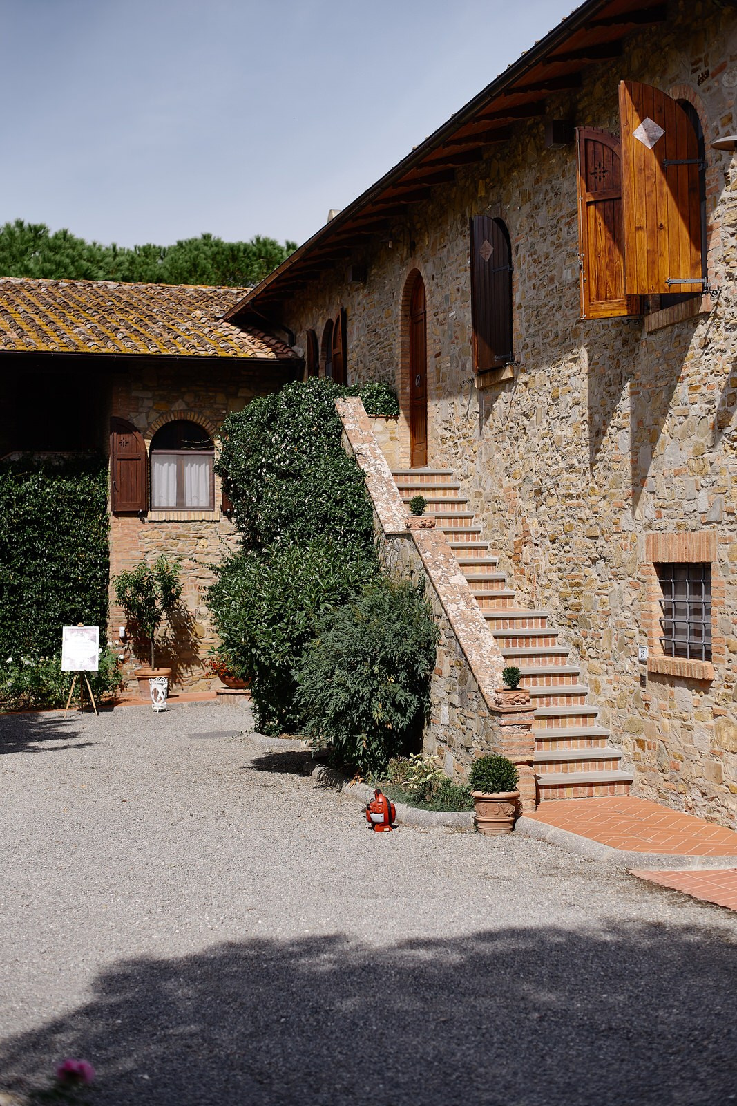 Stone courtyard of Villa Barbara agriturismo in Tuscany with external terracotta staircase, wooden shutters and lush green plants, decorated for a wedding