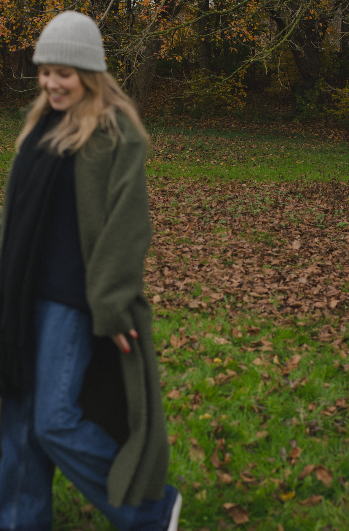 Porträt einer jungen Frau mit blonden Haaren und grauer Mütze vor einem Naturhintergrund