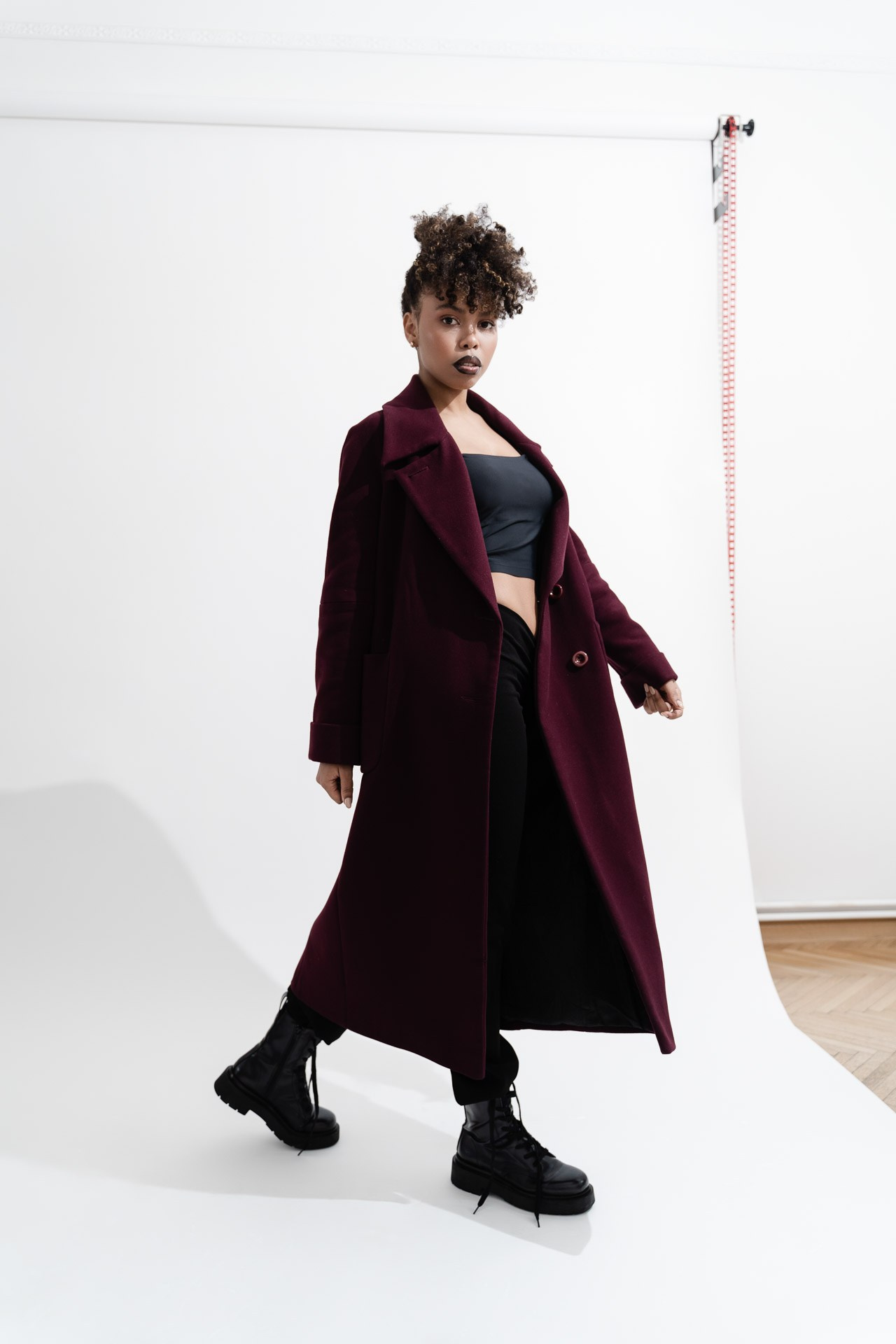Female model in burgundy coat walking in studio on white background
