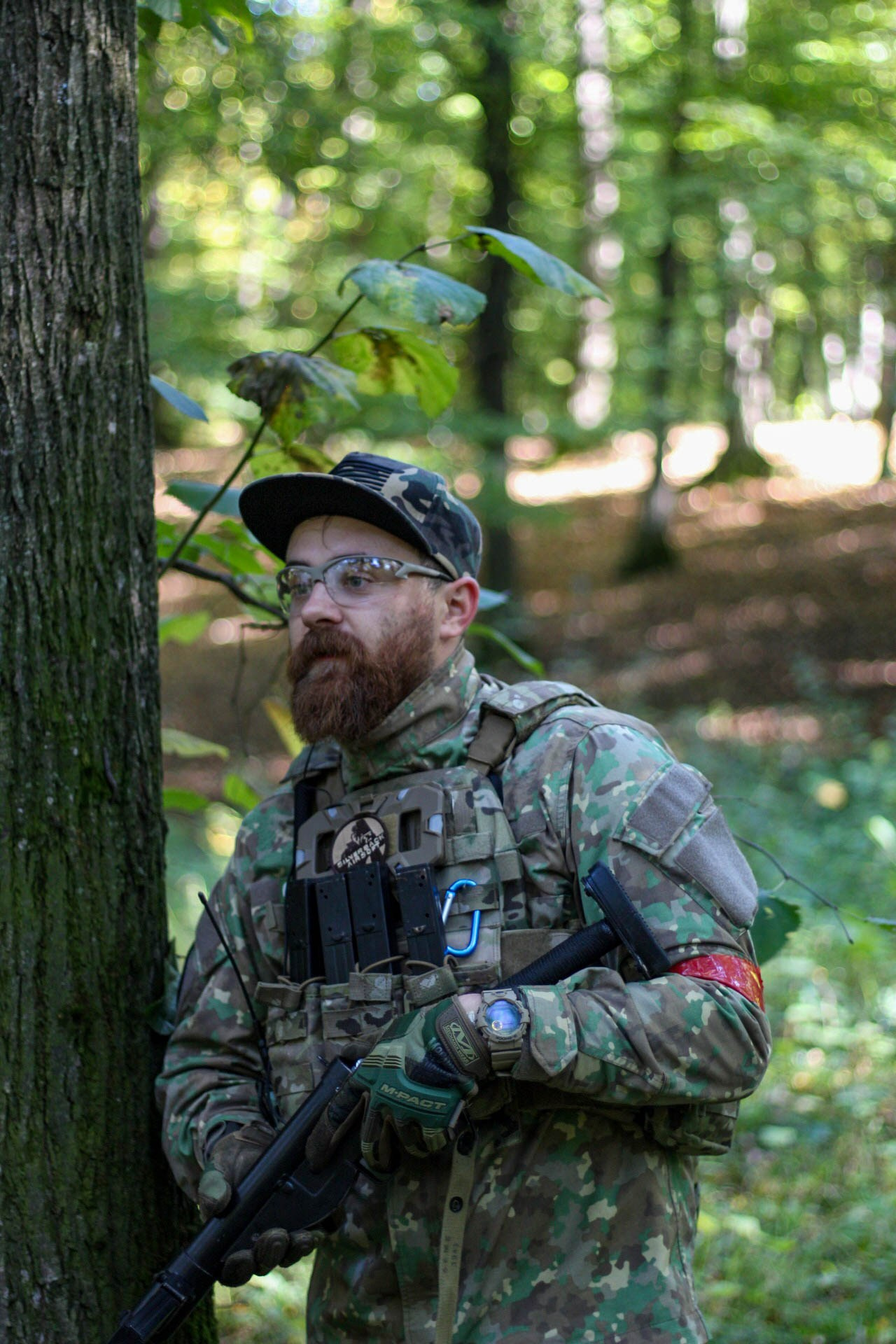 Portrait of a person dressed in camouflage gear, standing among tall trees in a dense forest.