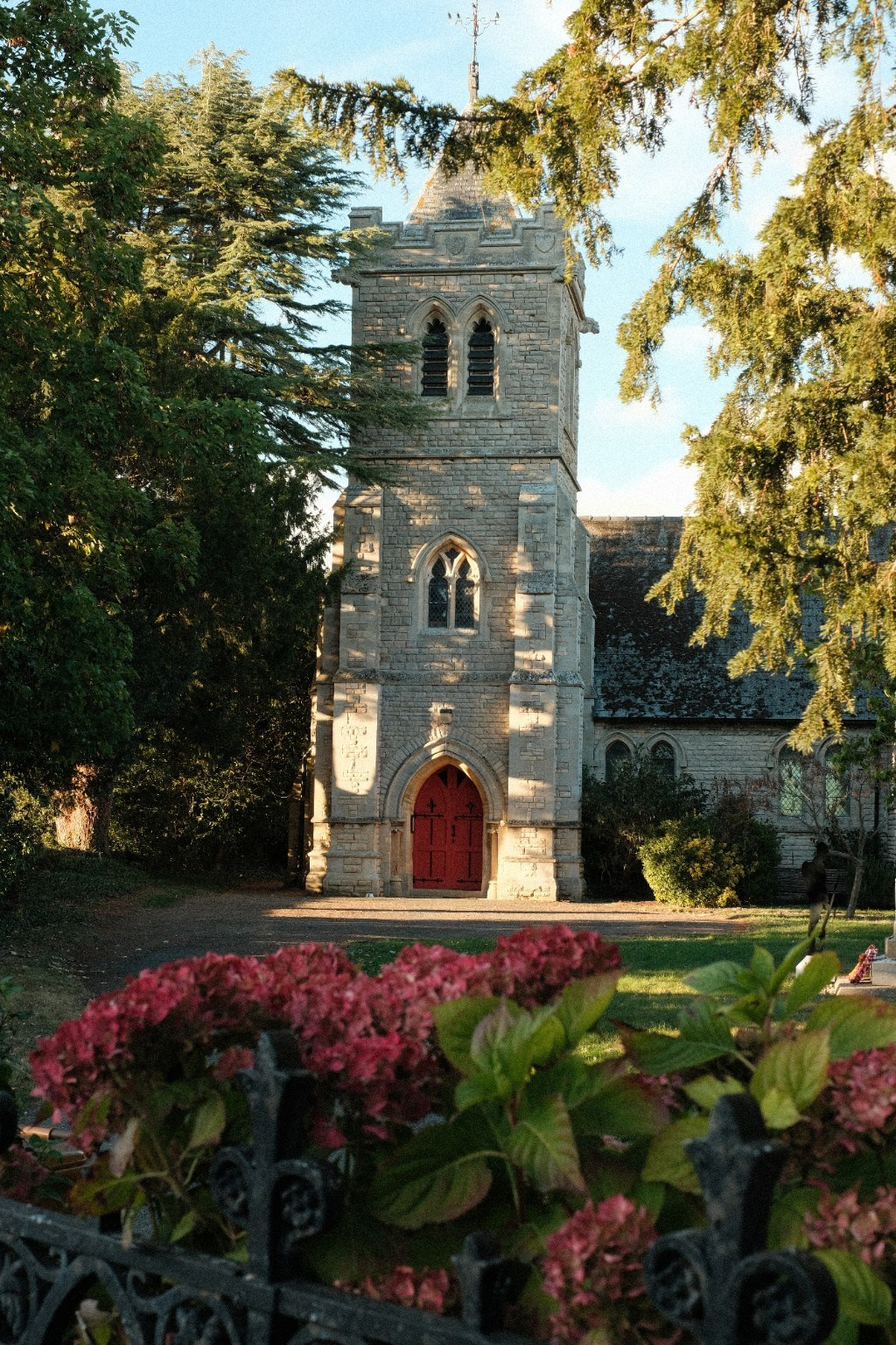 Stone church with a red door, framed by trees and flowers in warm light.