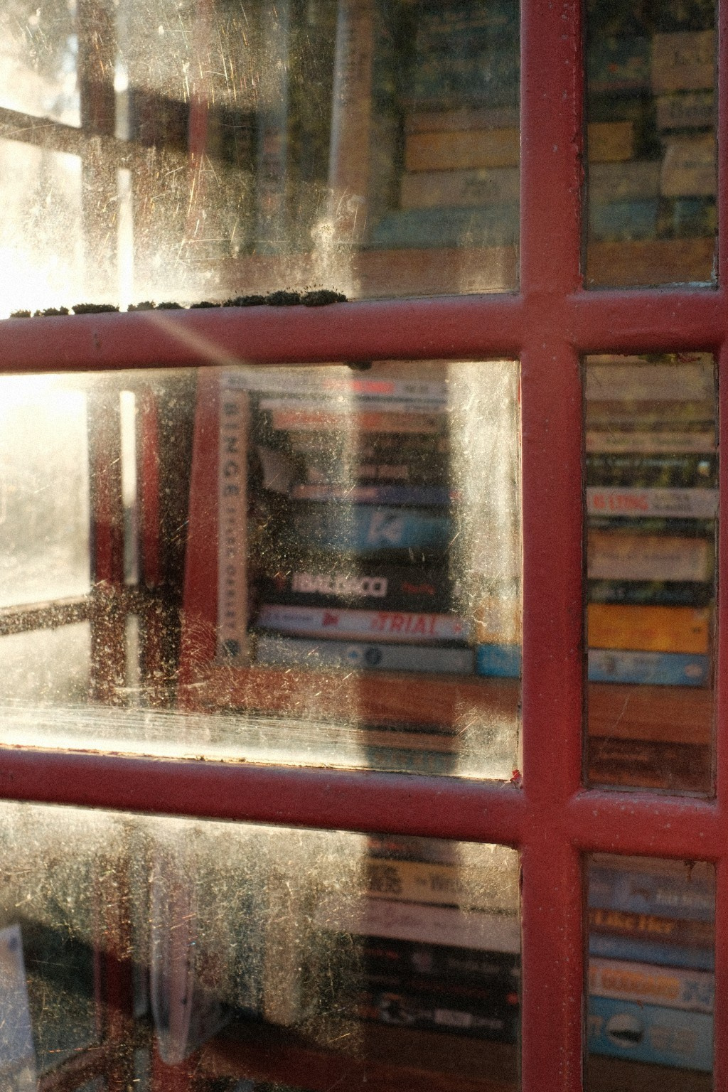 Reflections and sunlight on the window of a red telephone box.