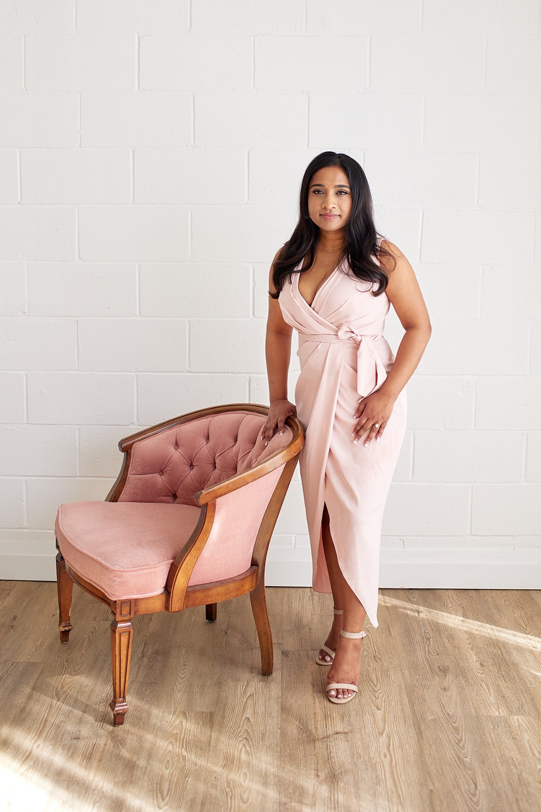 Women in pink dress poses beside pink chair