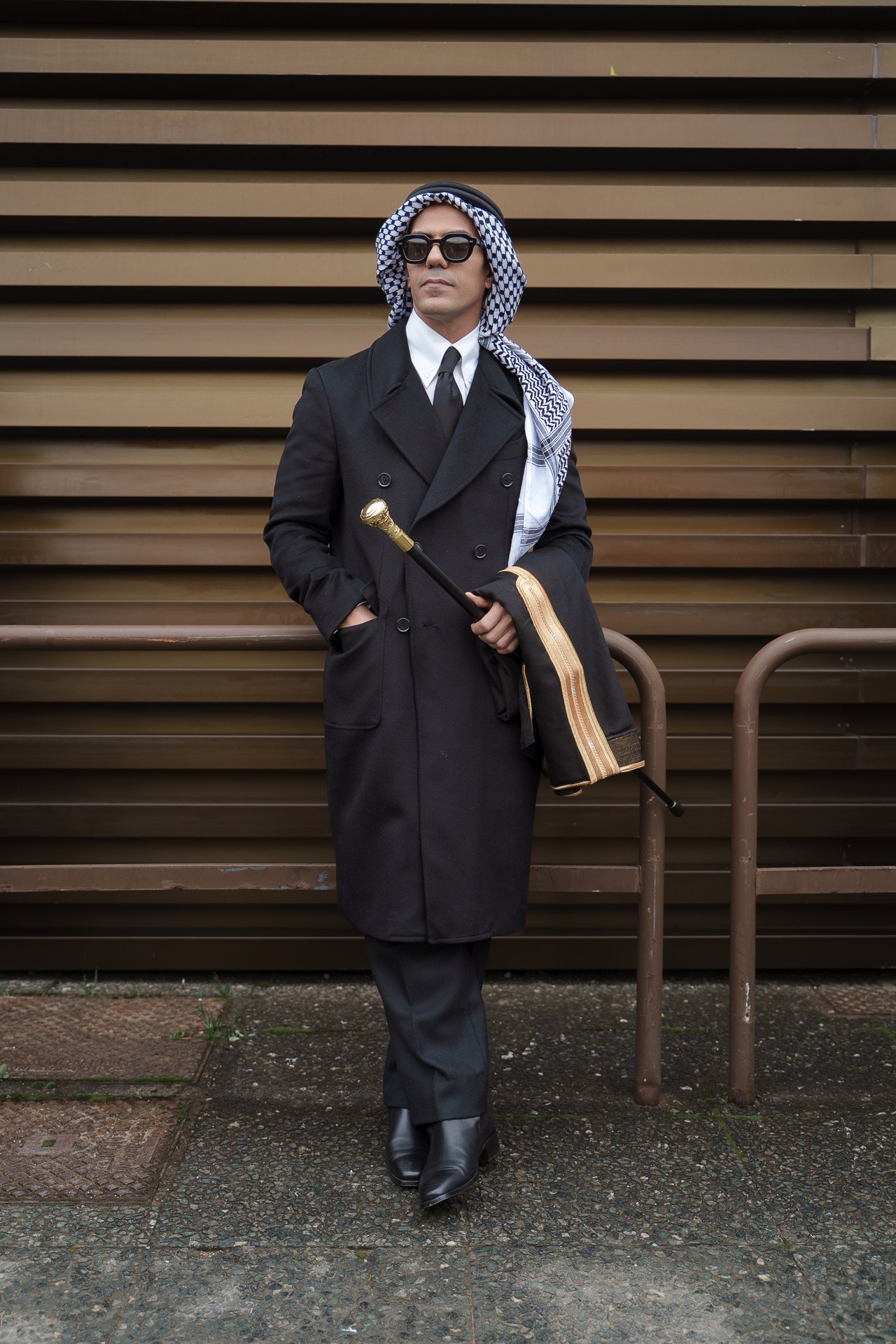 Man in black coat and keffiyeh holding cane at Pitti Uomo 109 Florence
