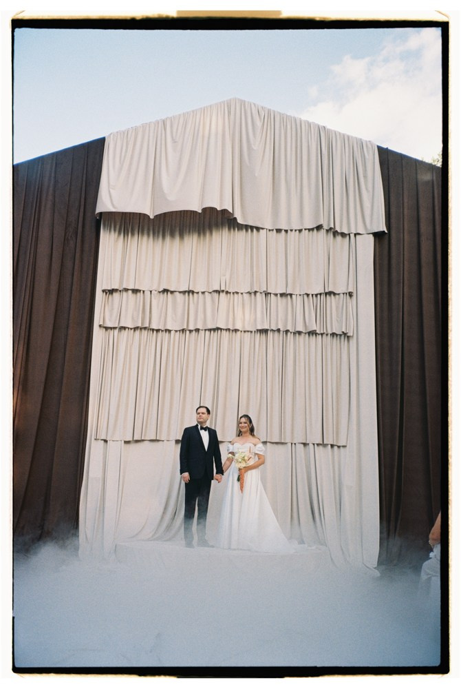 Couple standing before draped ceremony backdrop during destination wedding