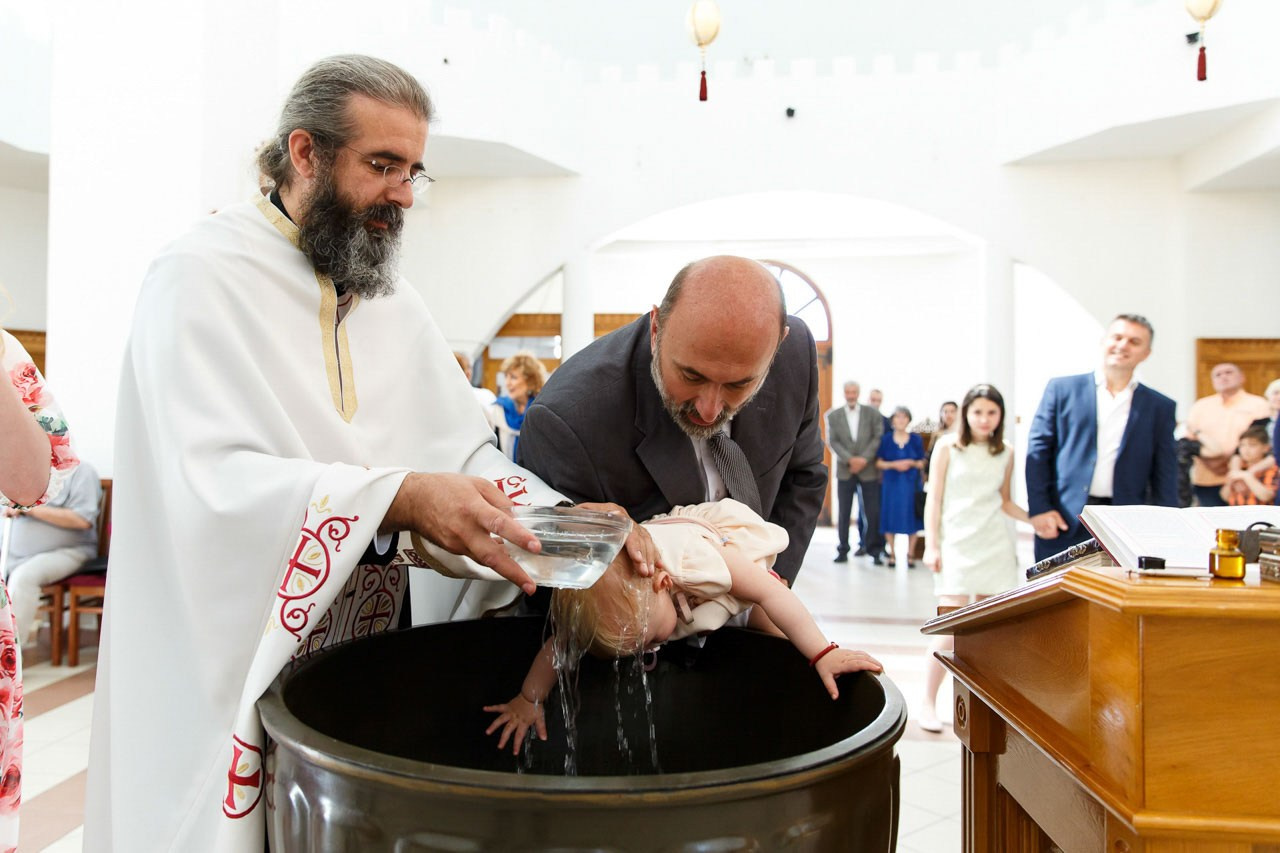 Sveštenik uranja bebu u svetu vodu tokom obreda.