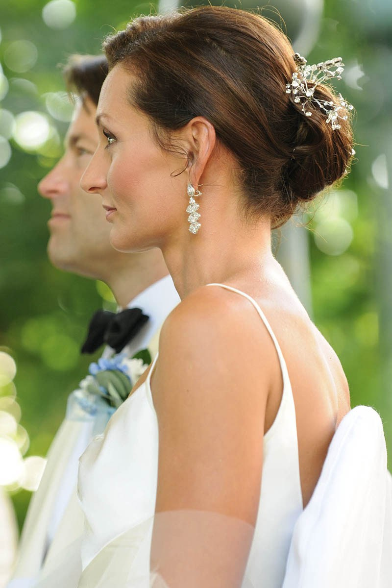 A stylish bride and groom in a white tuxedo listen as their outdoor wedding ceremony begins in Prague.