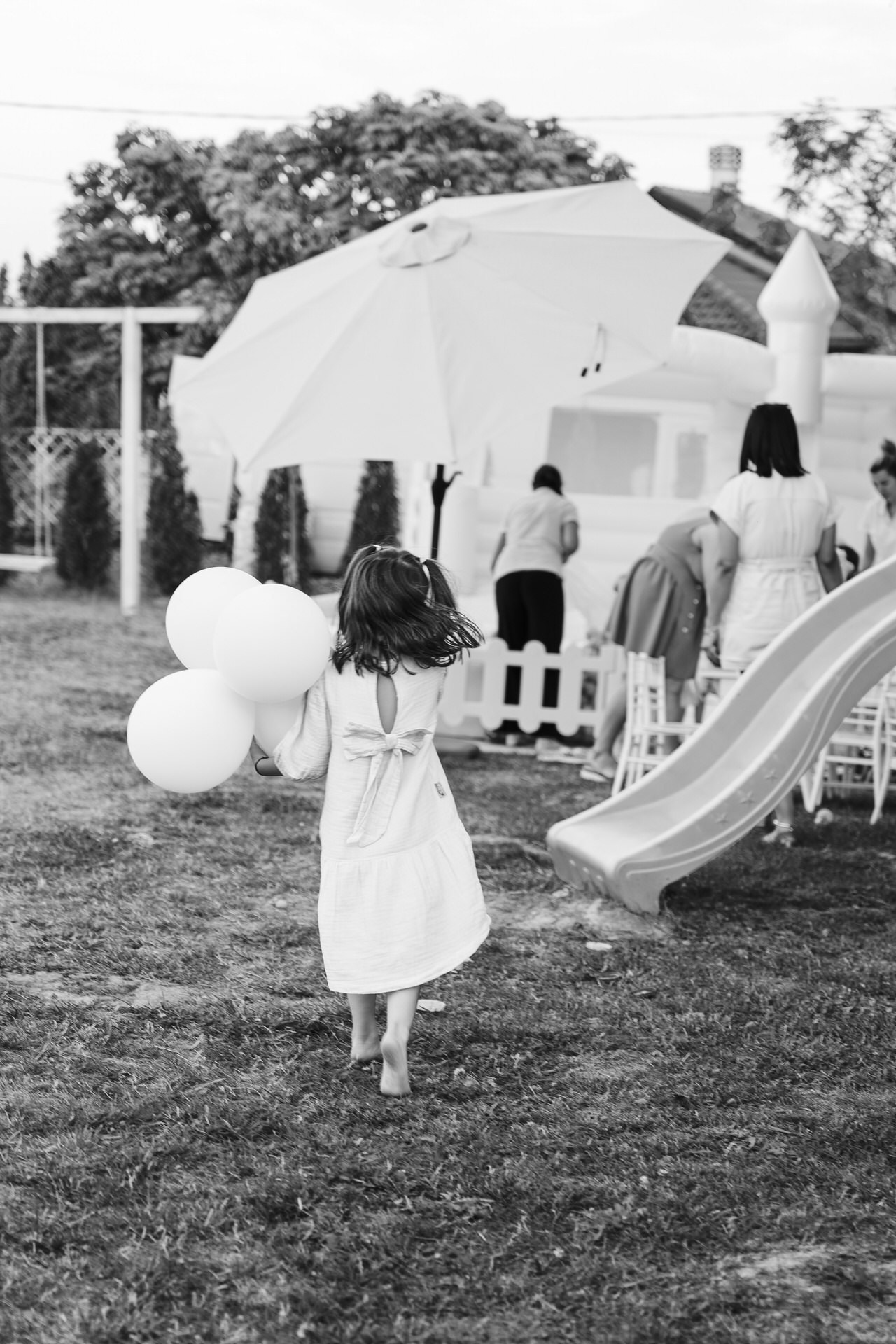 Crno-bela fotografija devojčice na travnjaku pored tobogana.
