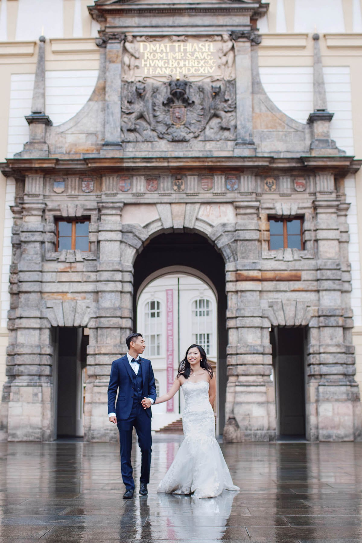Happy asian couple running through an archway of the Prague Castle in the rain