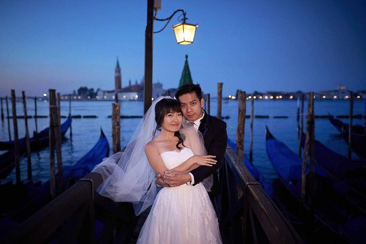 Daisy and Luis embracing above the gondola under a gas lamp in Venice.