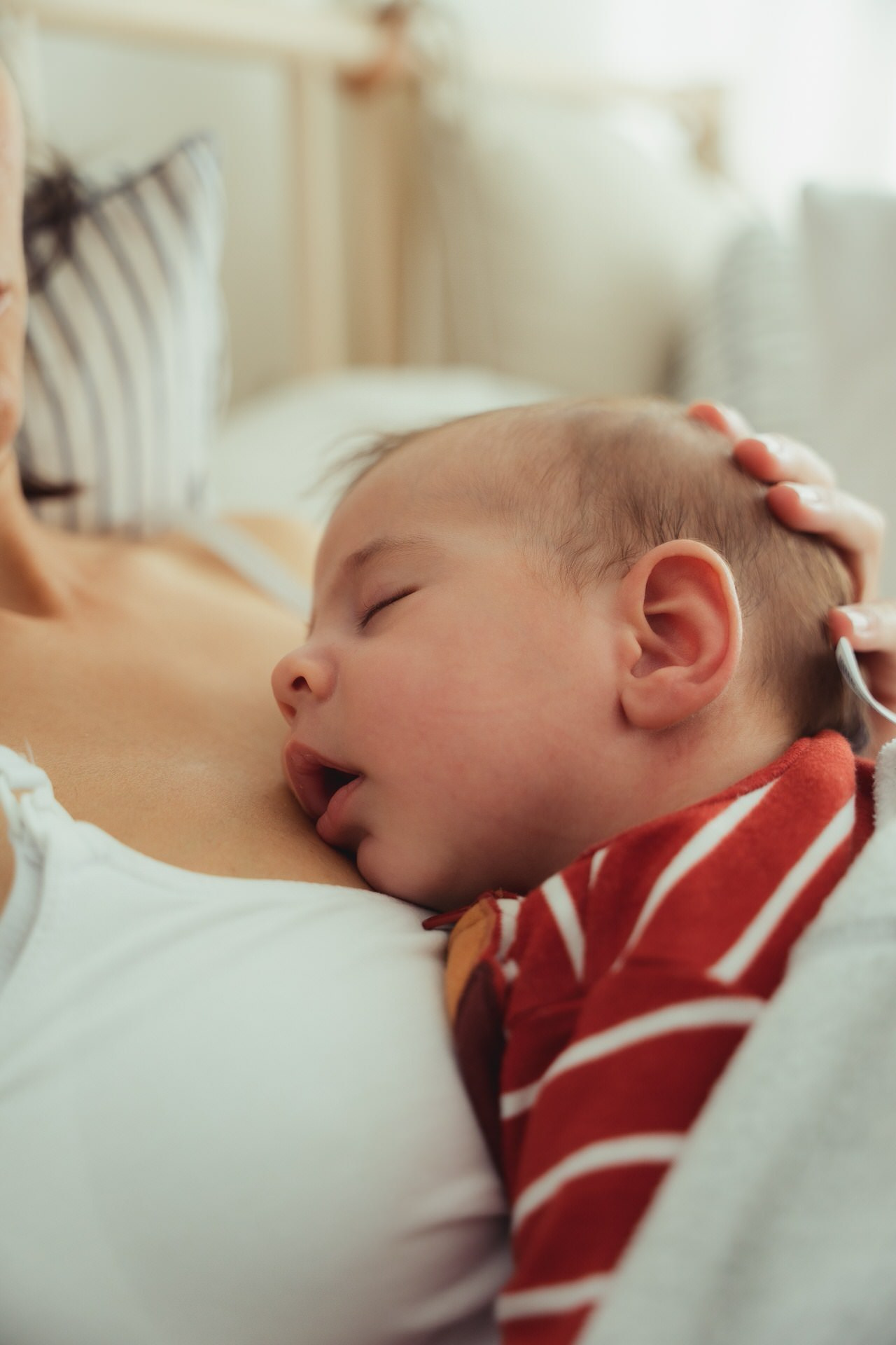 Beba spava naslonjena na grudi roditelja, dok je nežna ruka pridržava u toplom kućnom trenutku.