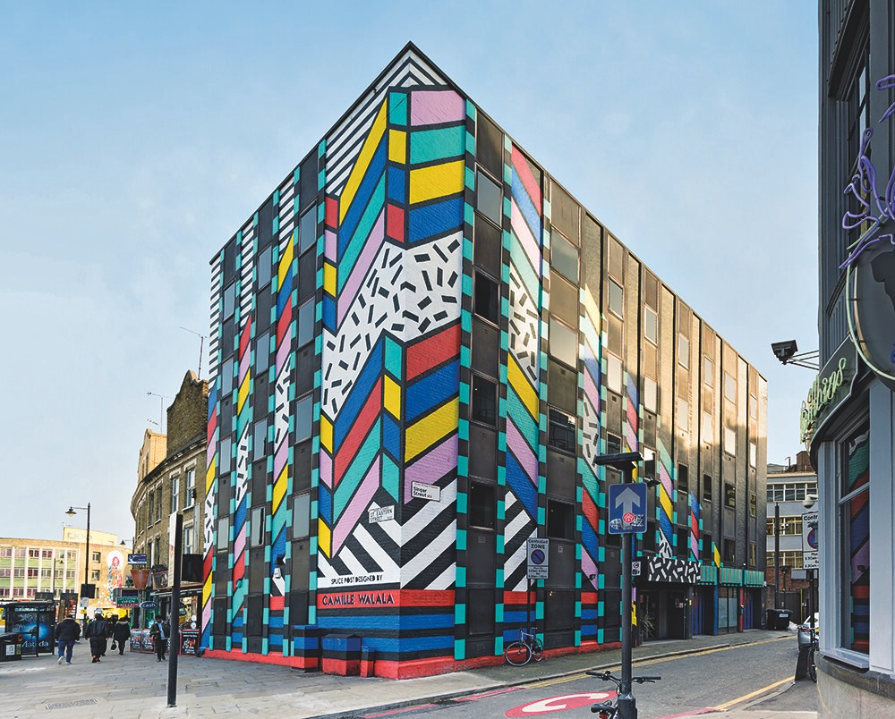 Мурал Dream Come True (2016) Камиль Валала в Восточном Лондоне, с чёрно-белыми полосами, неоновыми цветами и геометрическими узорами, отражает Memphis Revival, бросая вызов минимализму через игривую, антикапиталистическую эстетику.
