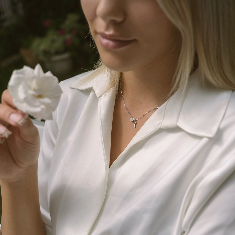 Zlatna ogrlica na devojci u beloj košulji koja drži cvet.