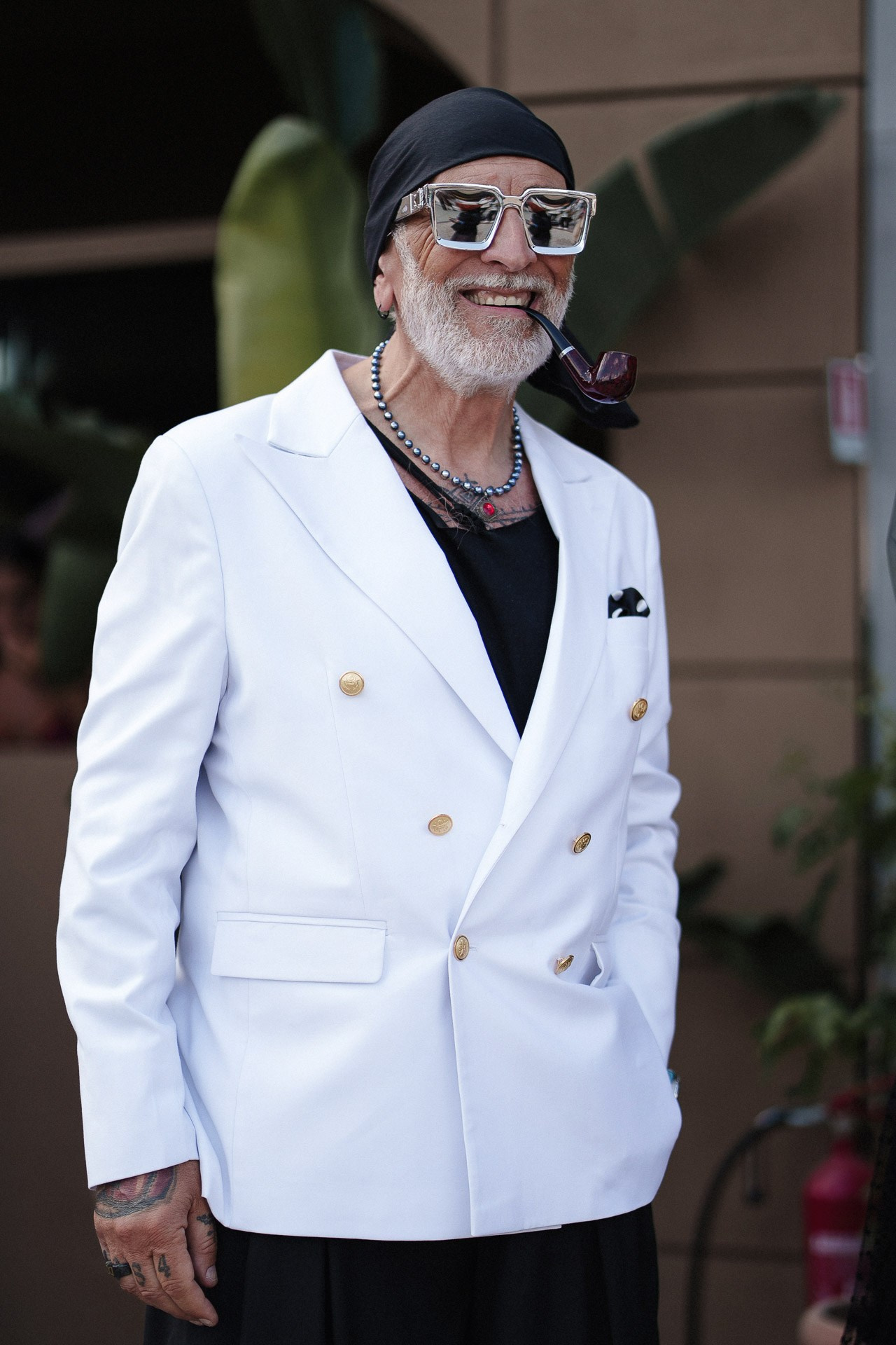 Pitti Uomo 110 street style portrait, guest in white double-breasted blazer, pipe and bold sunglasses