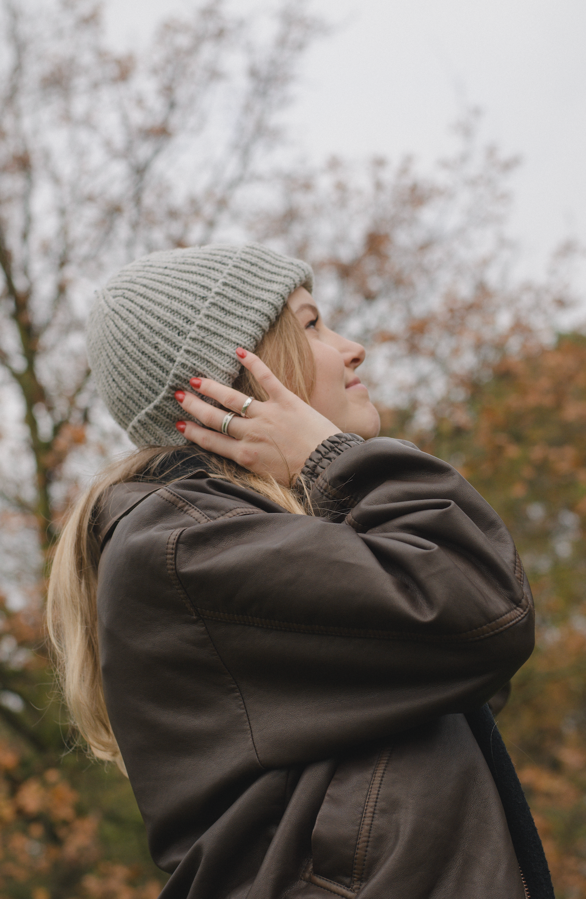 Seitenprofil Porträt einer jungen Frau mit blonden Haaren und grauer Mütze vor einem Naturhintergrund