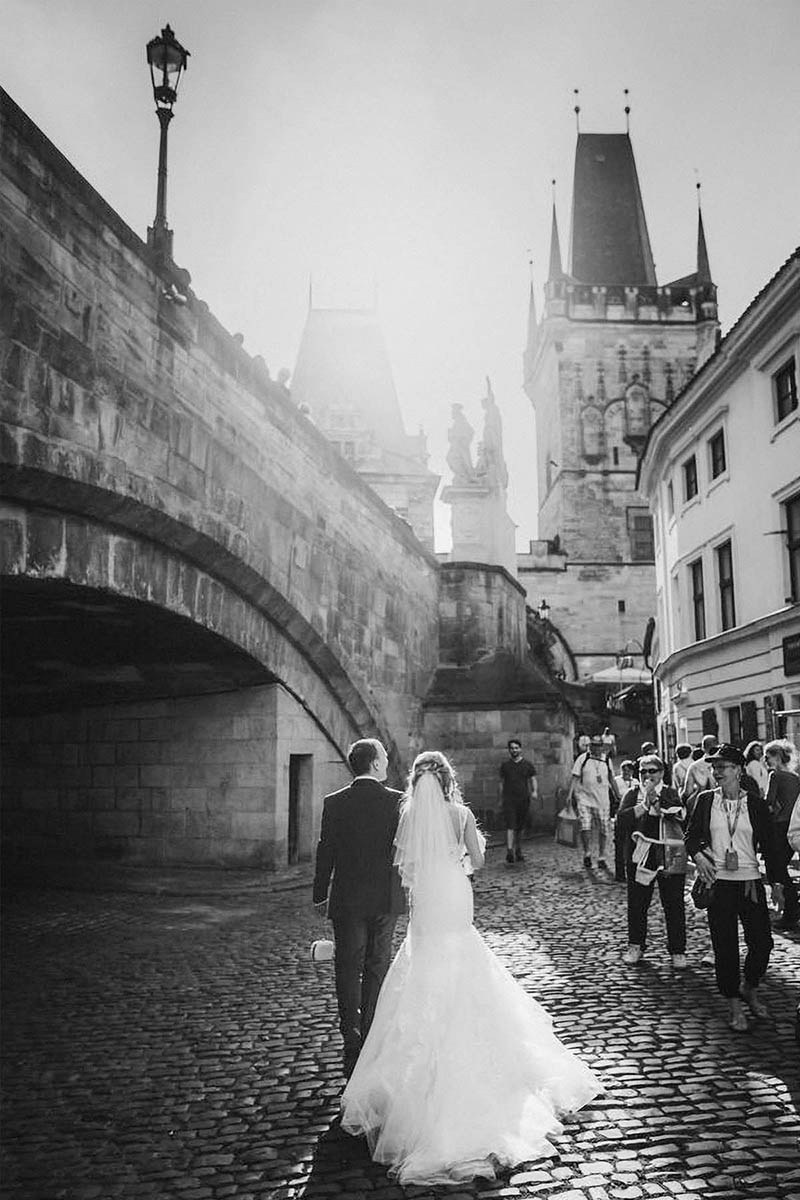 The bride and groom are cheered by onlookers as they walk hand-in-hand under the Charles Bridge.