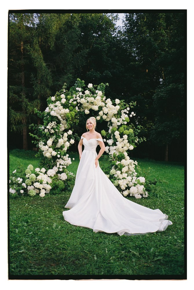 Bride standing by floral arch during outdoor wedding ceremony