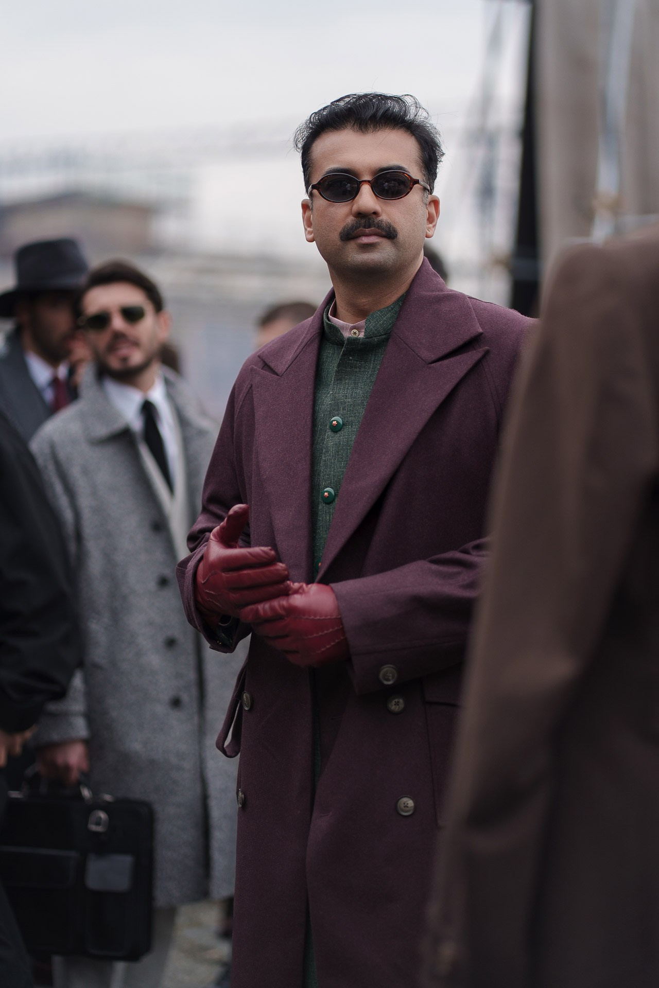 Man in burgundy coat and red gloves wearing sunglasses at Pitti Uomo Florence