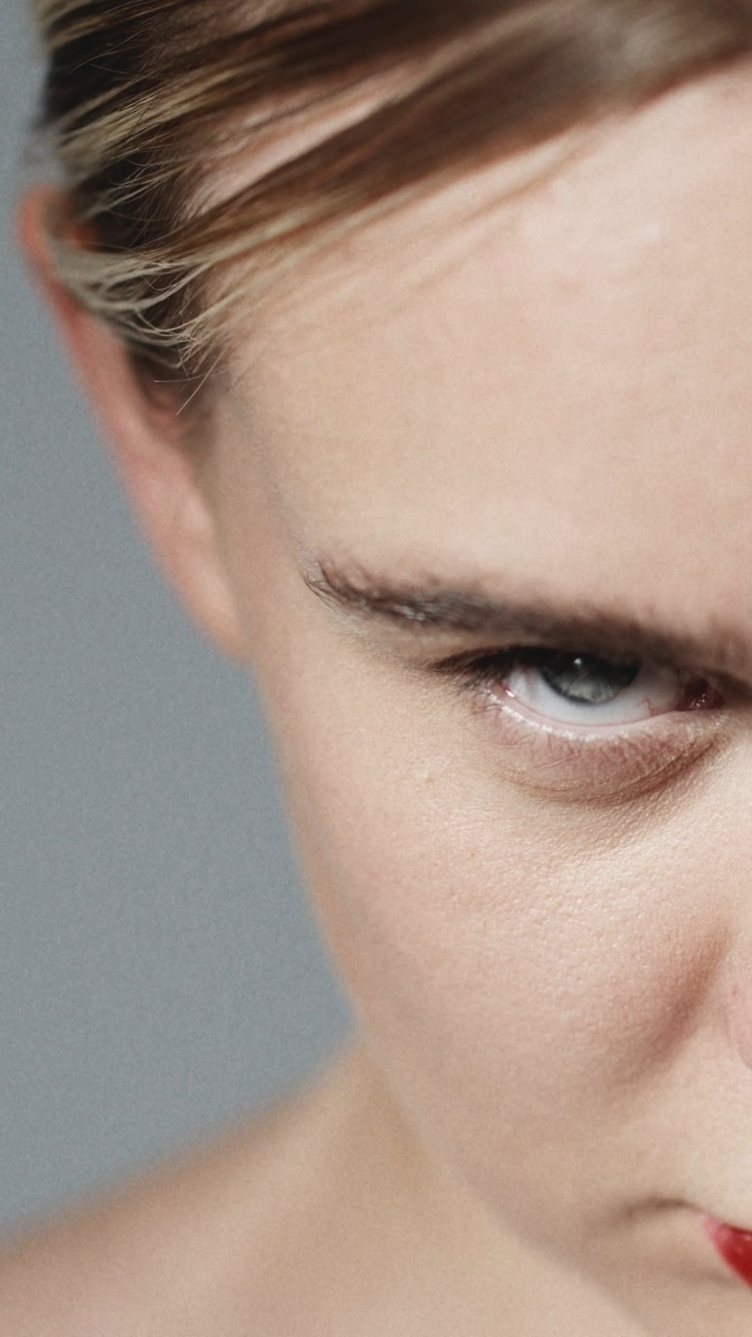 A dramatic close-up of a woman’s face with a piercing gaze, emphasizing her furrowed brow and intense expression, with soft lighting.