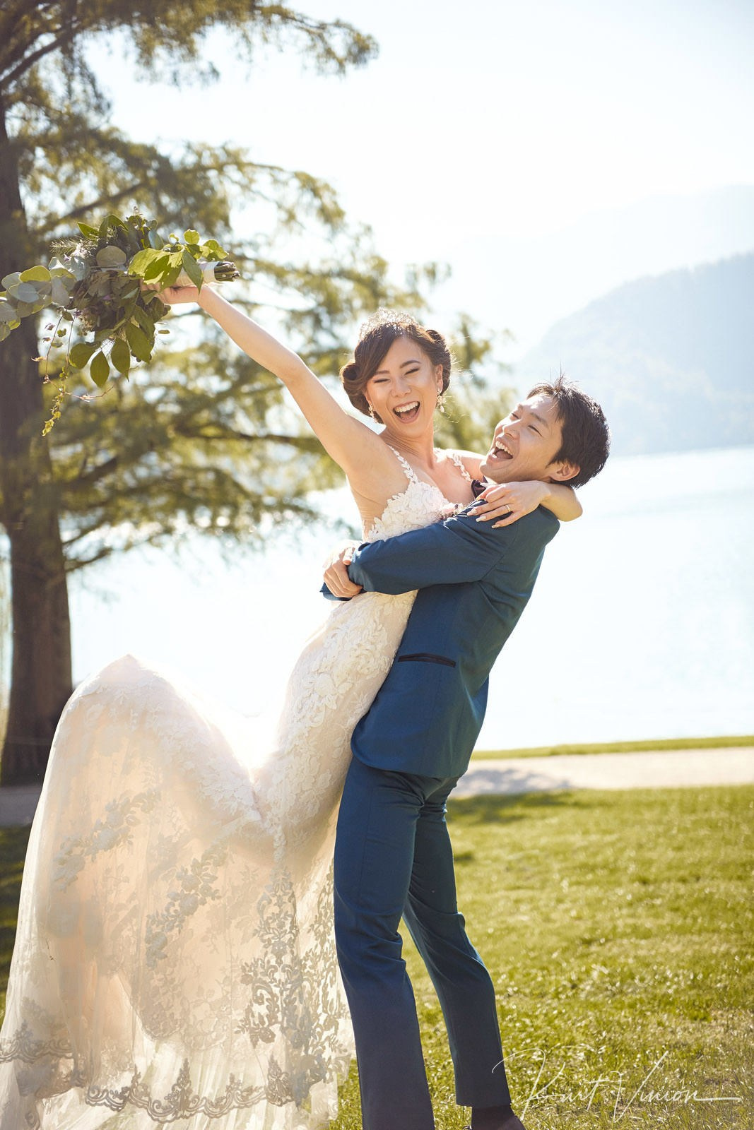 Groom lifting joyful bride near Lake Bled shore portrait.