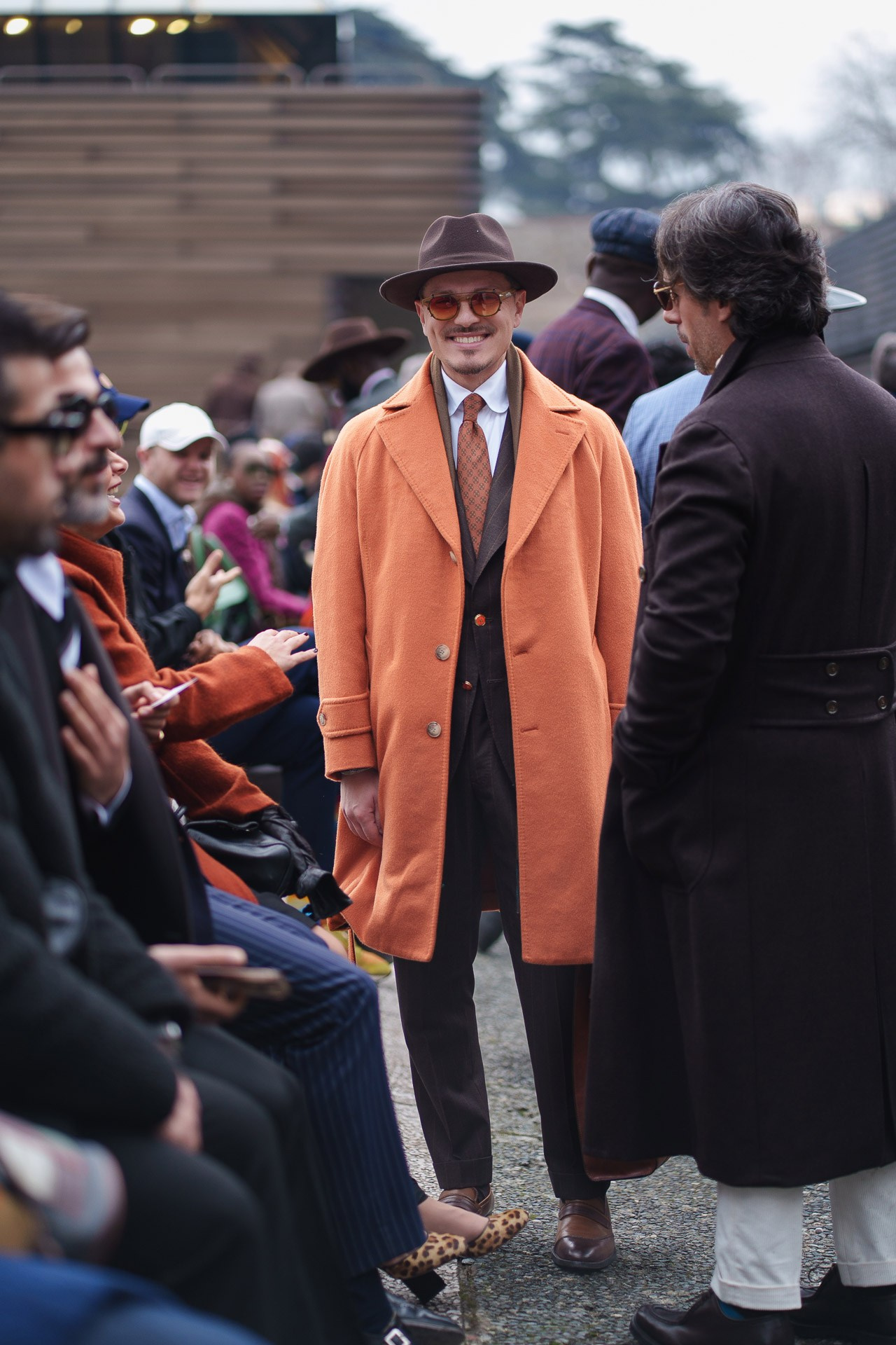 Man in orange overcoat standing among crowd at Pitti Uomo 109 Florence