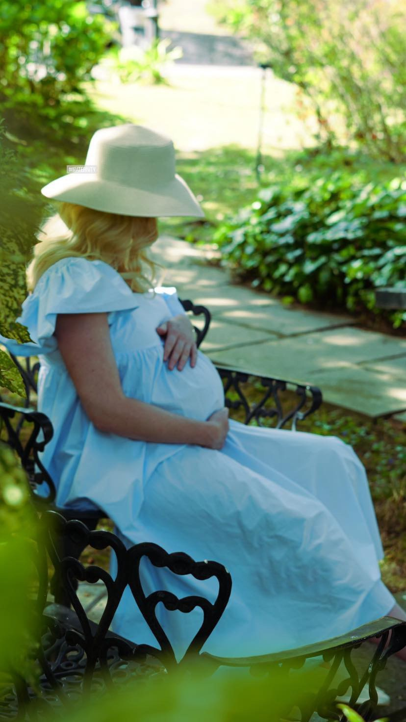 Donna incinta che posa in un parco, circondata da luce naturale soffusa e dal verde.