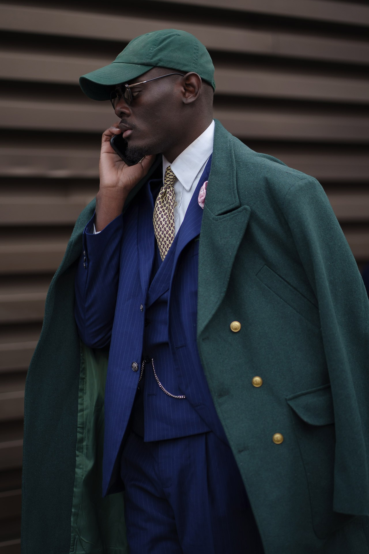 Man in green cap and tailored blue suit talking on phone at Pitti Uomo Florence